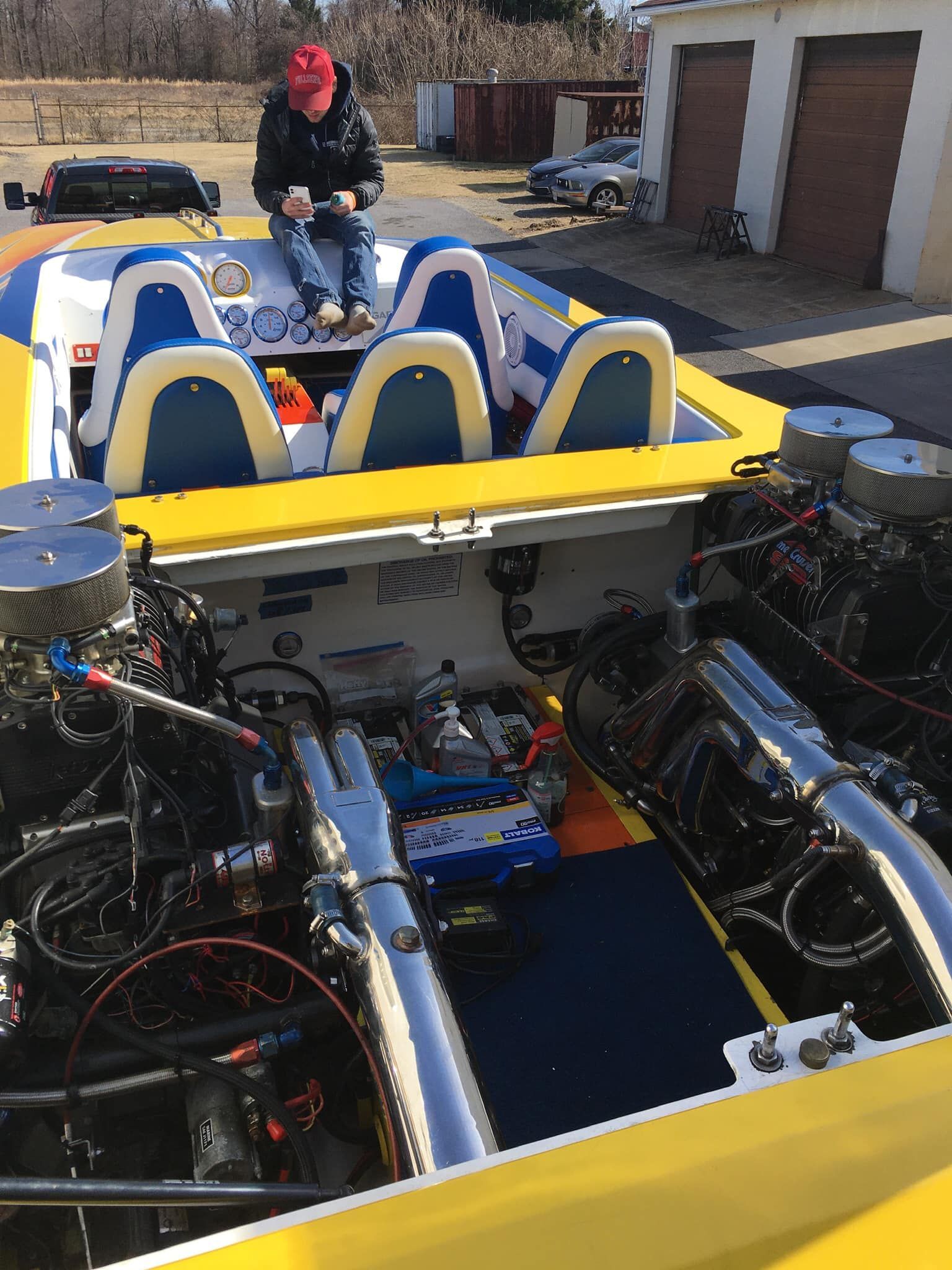 Person sitting on the deck of a yellow, blue, and white speed boat with exposed engine components.