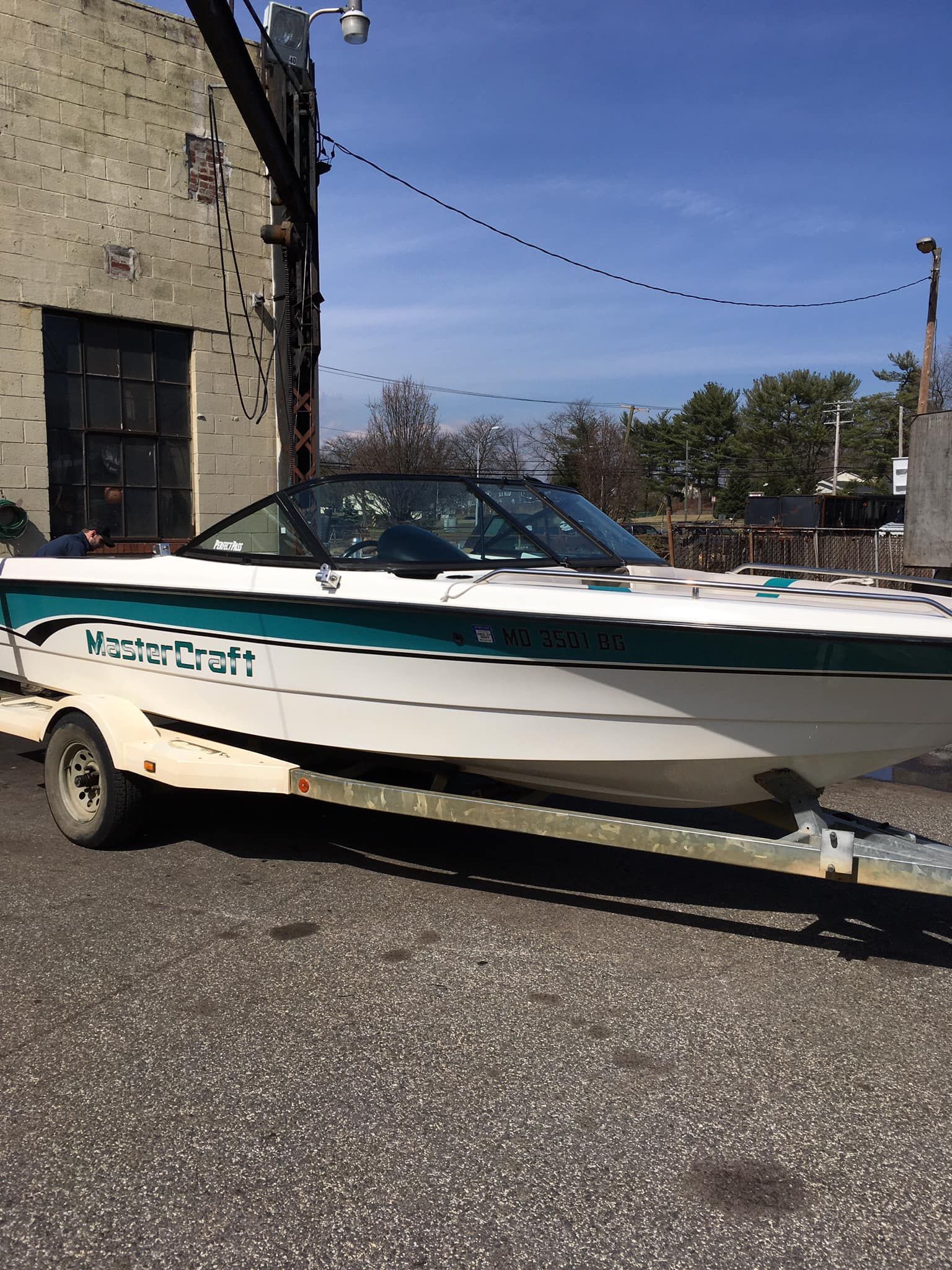 Boat on trailer next to brick building. White and teal with 