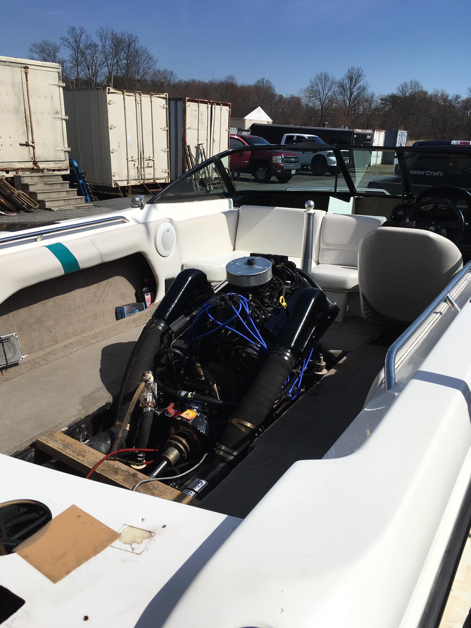 Boat interior with a large black engine, white seats, and a clear windshield; outdoors.