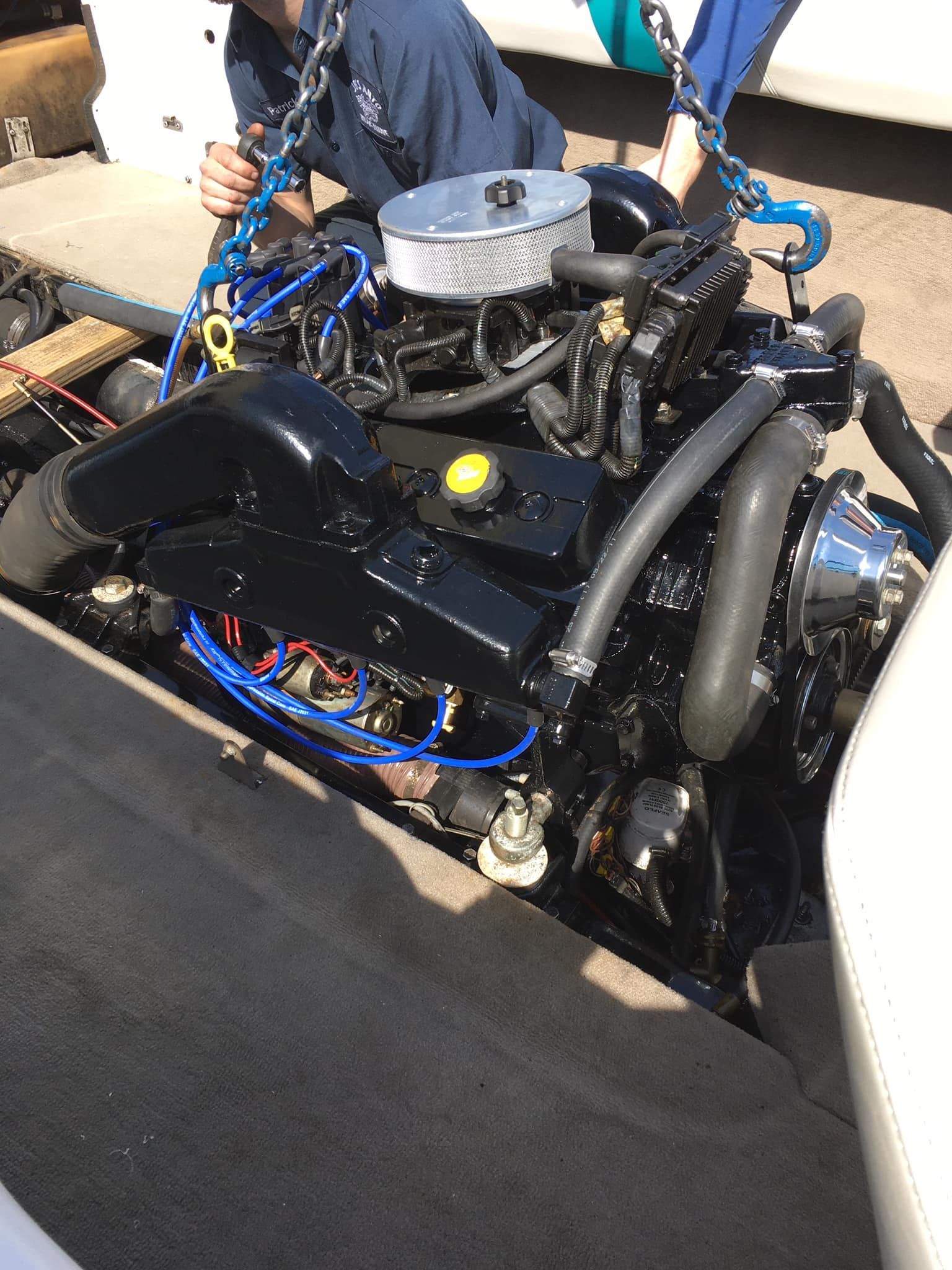 Black boat engine being lifted, two people nearby.