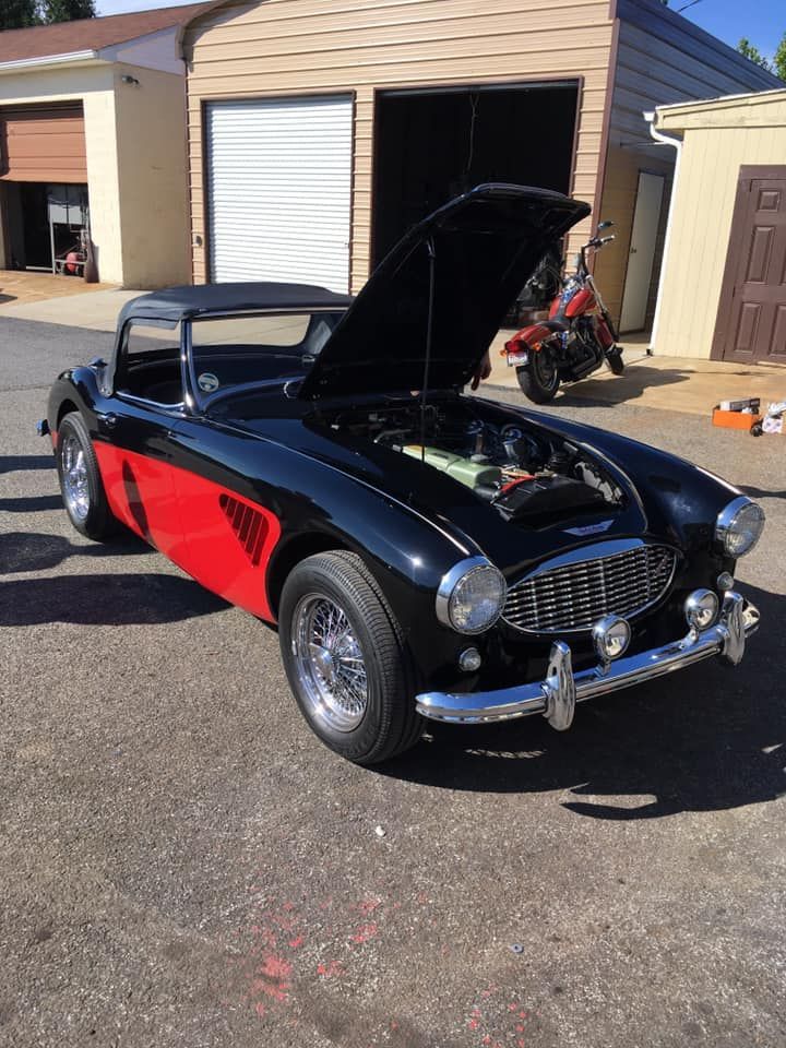 Black and red vintage sports car with hood open, parked in front of a garage.