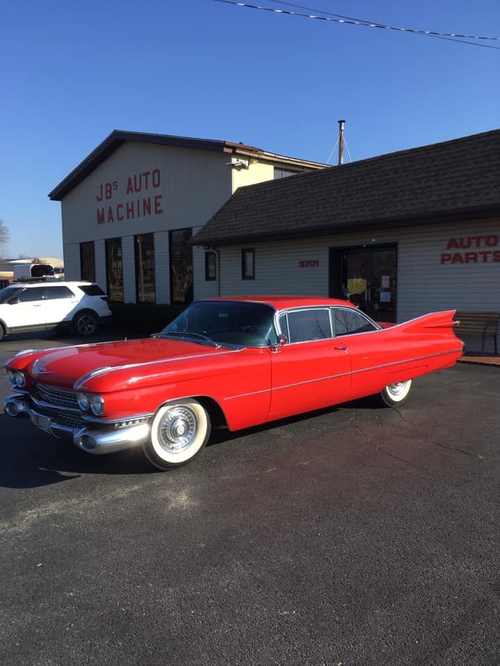 Red classic Cadillac in front of an auto parts store, sunny day.