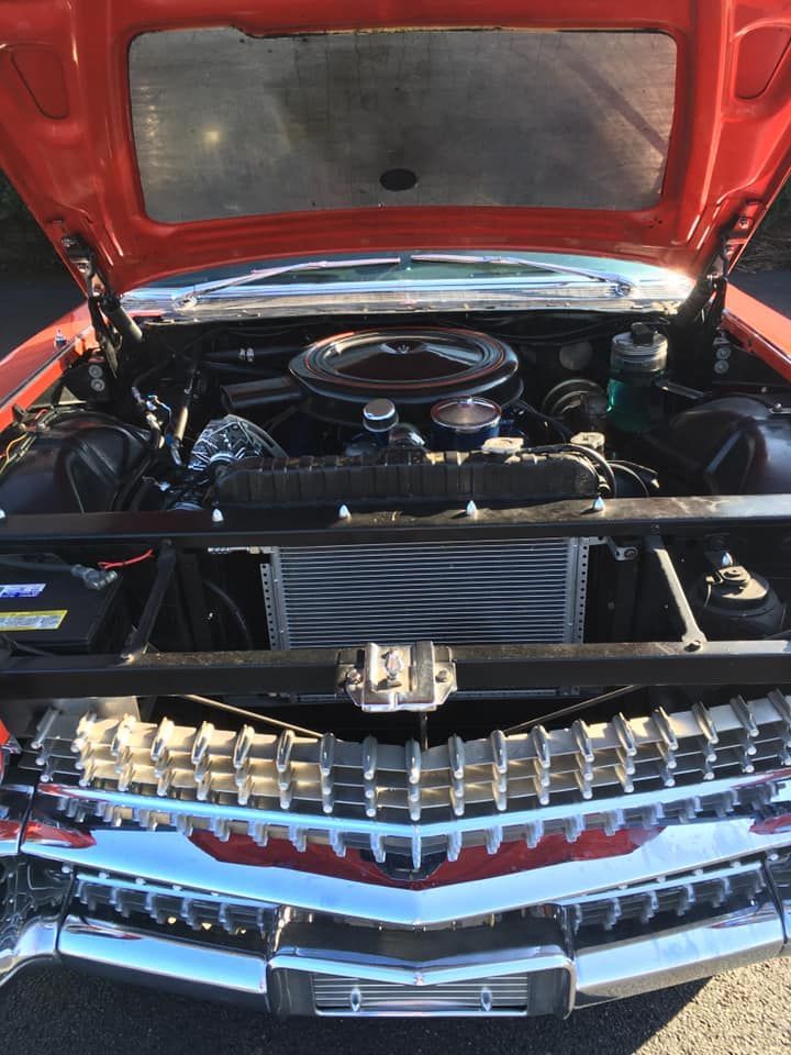 Open hood of a classic red Cadillac. Chrome grille, black engine bay, and shiny components are visible.