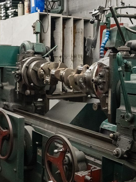 A crankshaft being ground on a green machine in a workshop.