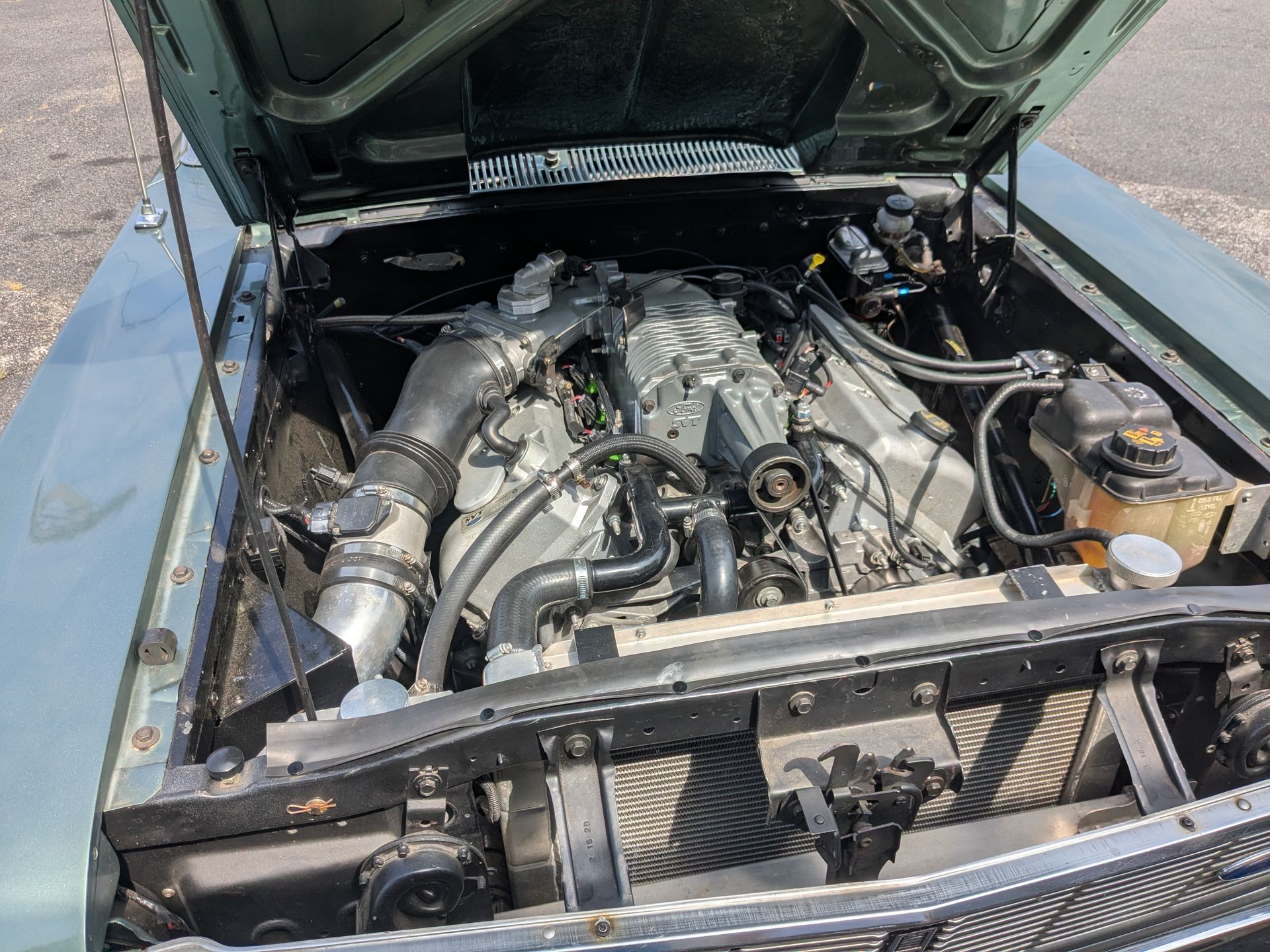 Open car hood showing a modified engine bay with hoses, pipes, and a front radiator support