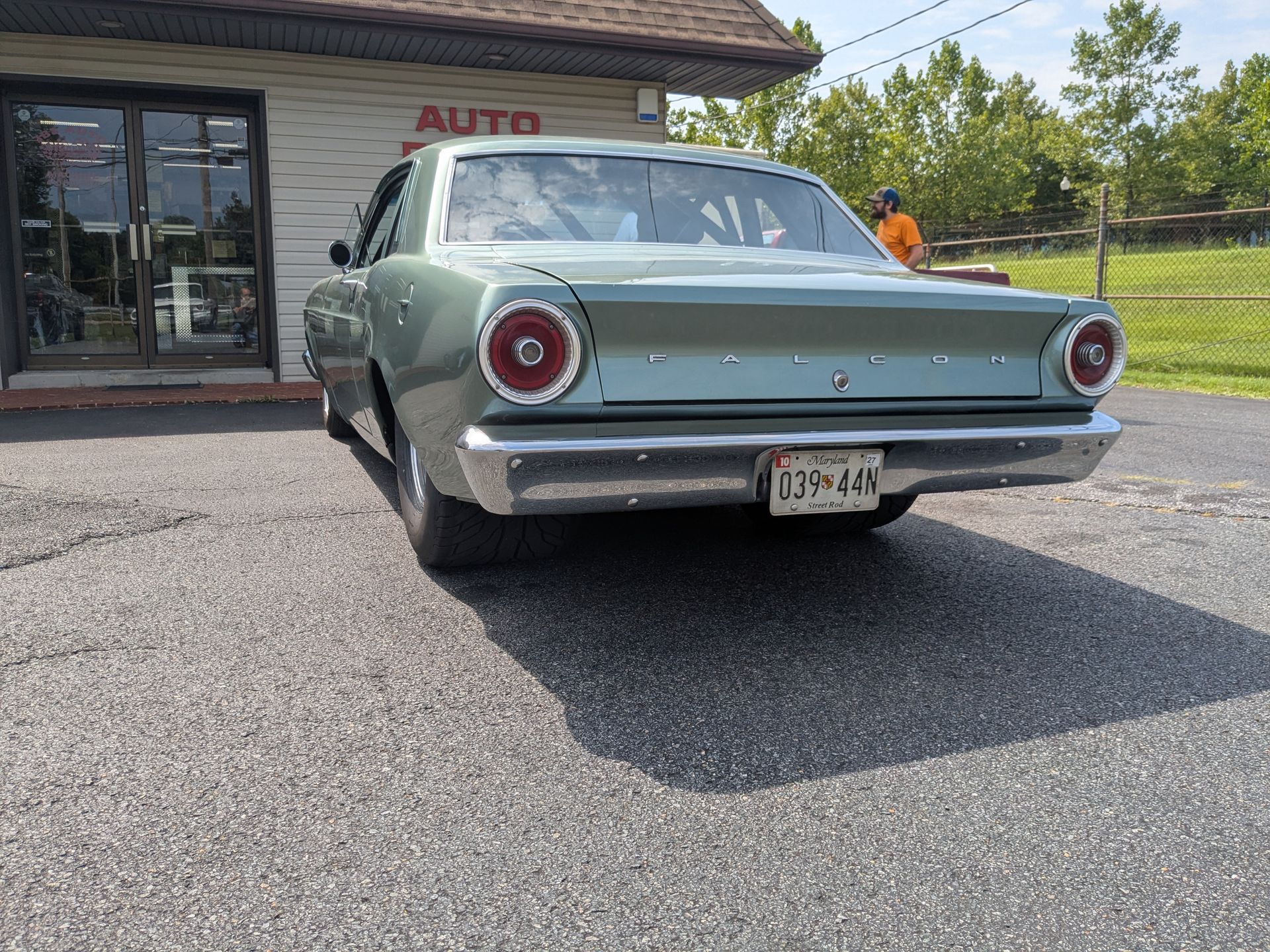 Vintage pale green car parked outside an auto shop on a sunny day