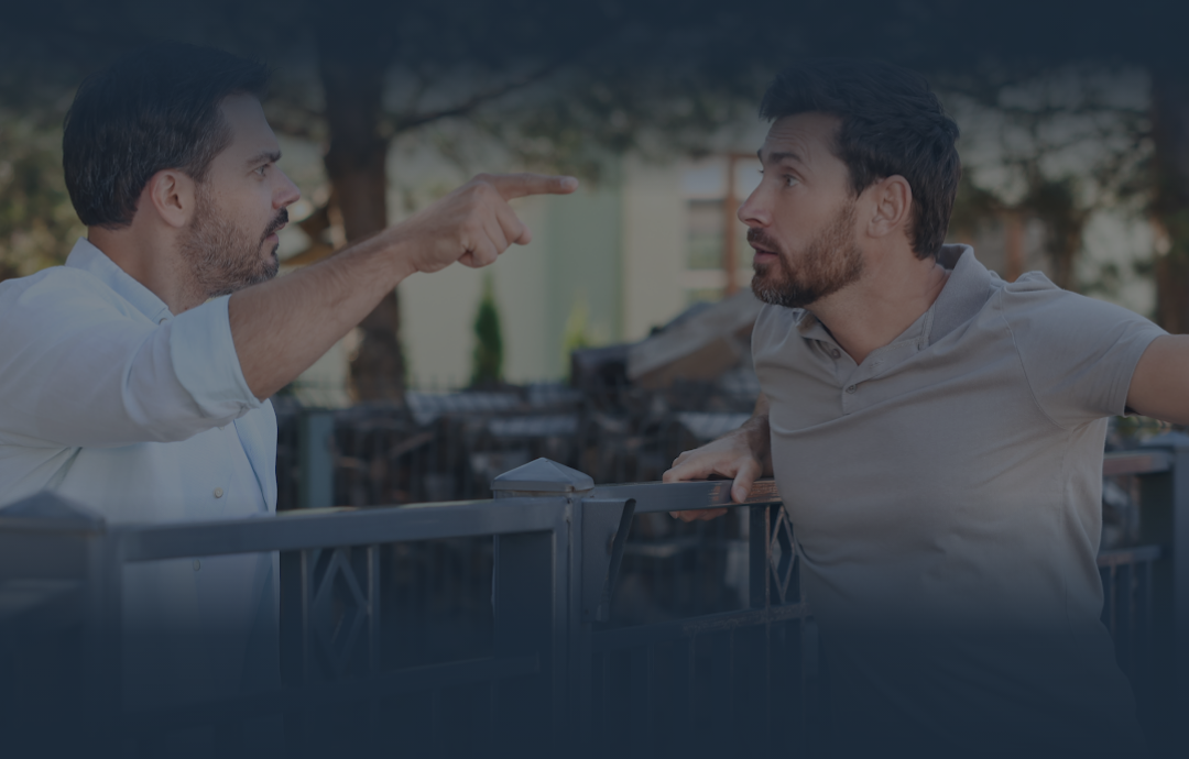Two men arguing at a café table, one pointing angrily at the other.
