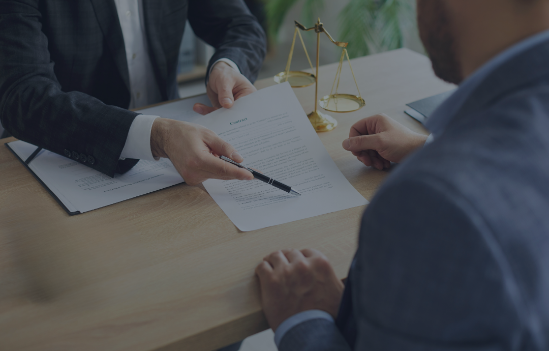 Lawyer pointing to a document for a client at a desk, scales of justice in the background.
