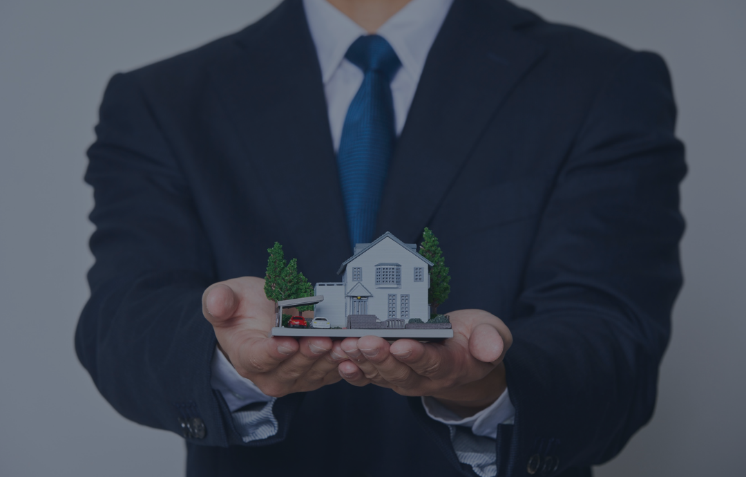 Person in a suit holding a miniature house, representing property ownership.