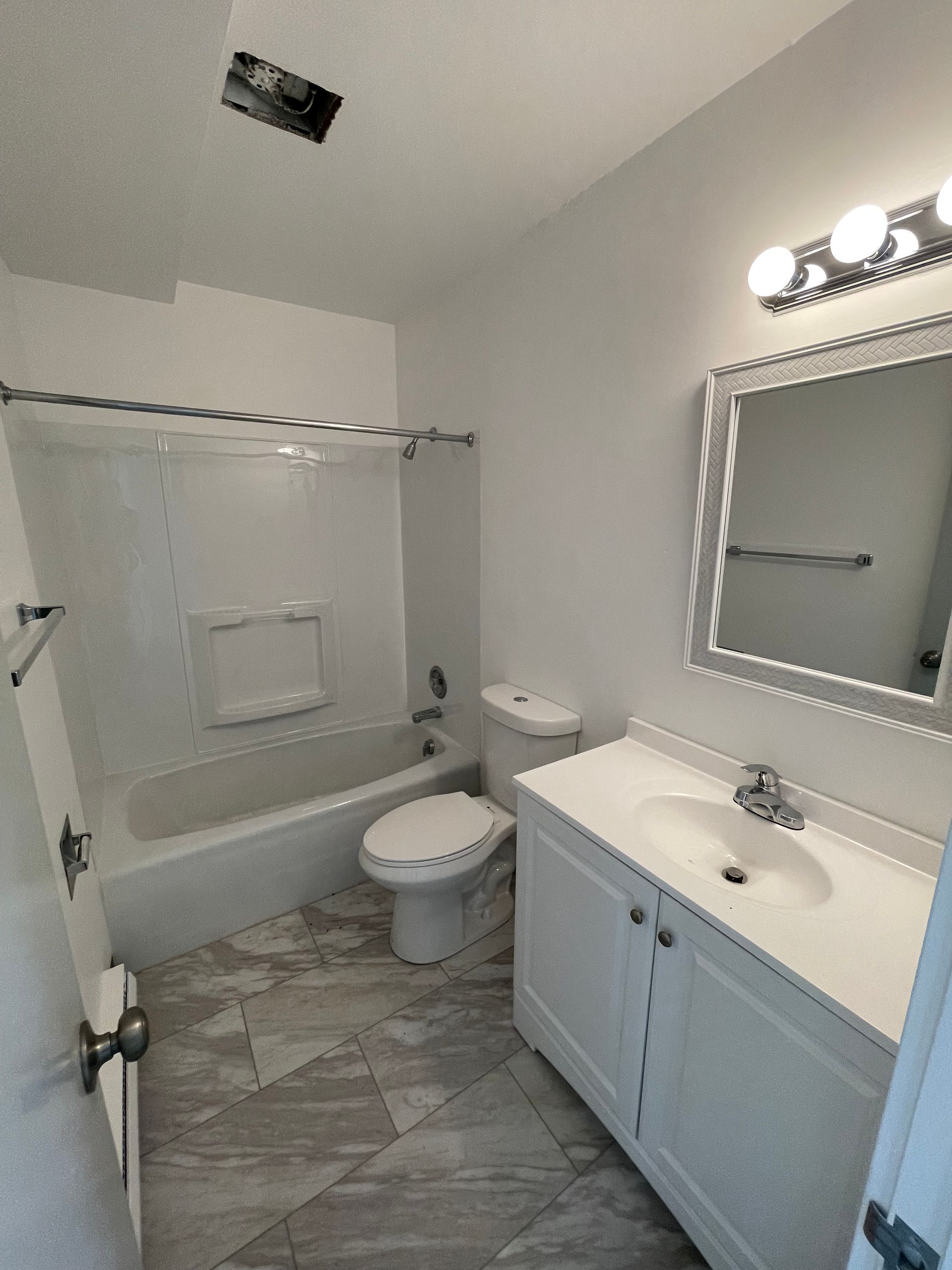 White bathroom with a tub, toilet, and sink, light grey tile floor.