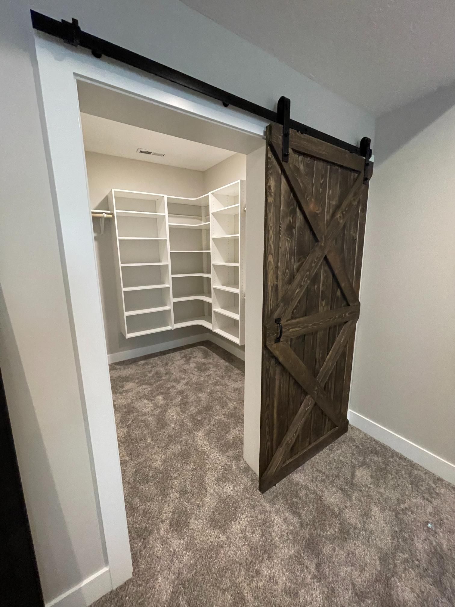 Barn door opening to a walk-in closet with white shelving and gray carpet.