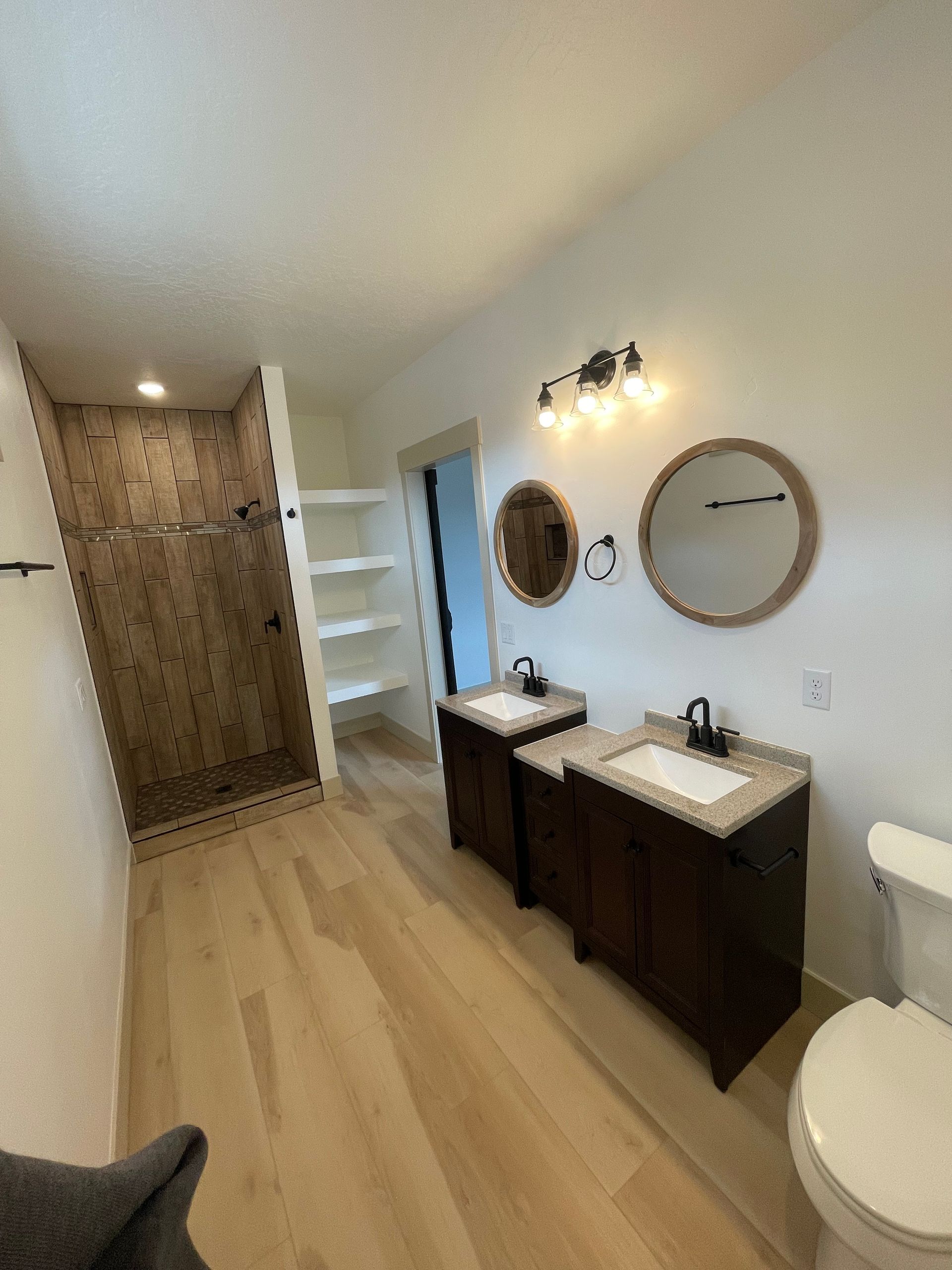 Bathroom with two vanities, a wooden shower, and a toilet. Beige wood-look floor, white walls.