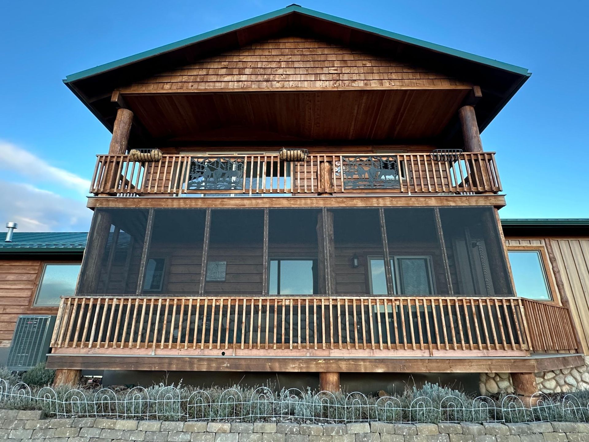 Two-story log cabin with screened porch, wooden railings, and blue sky.