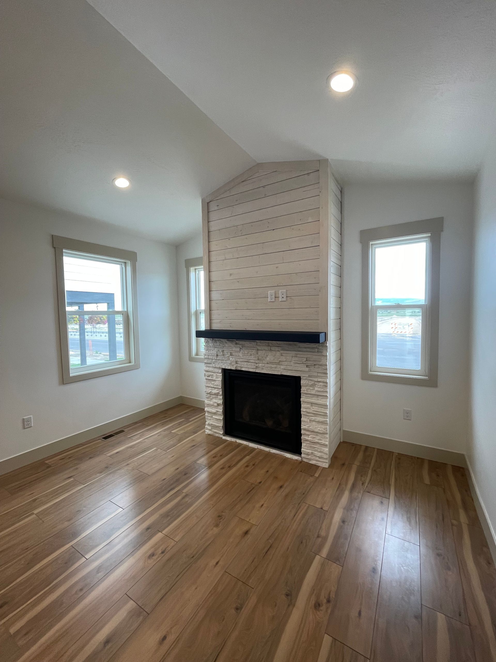 Room with fireplace, light wood floors, two windows, and white brick chimney.