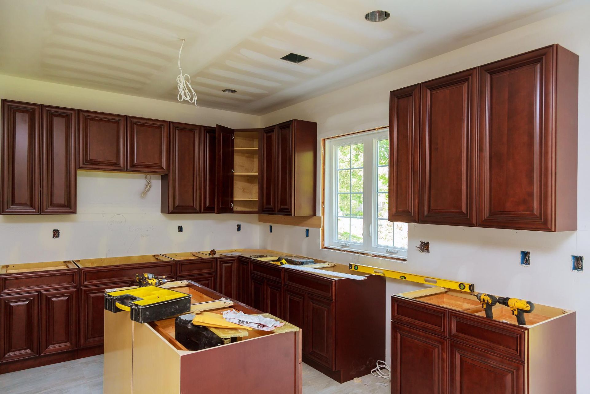 Kitchen under construction, with dark wood cabinets, a window, and tools visible on the counters.