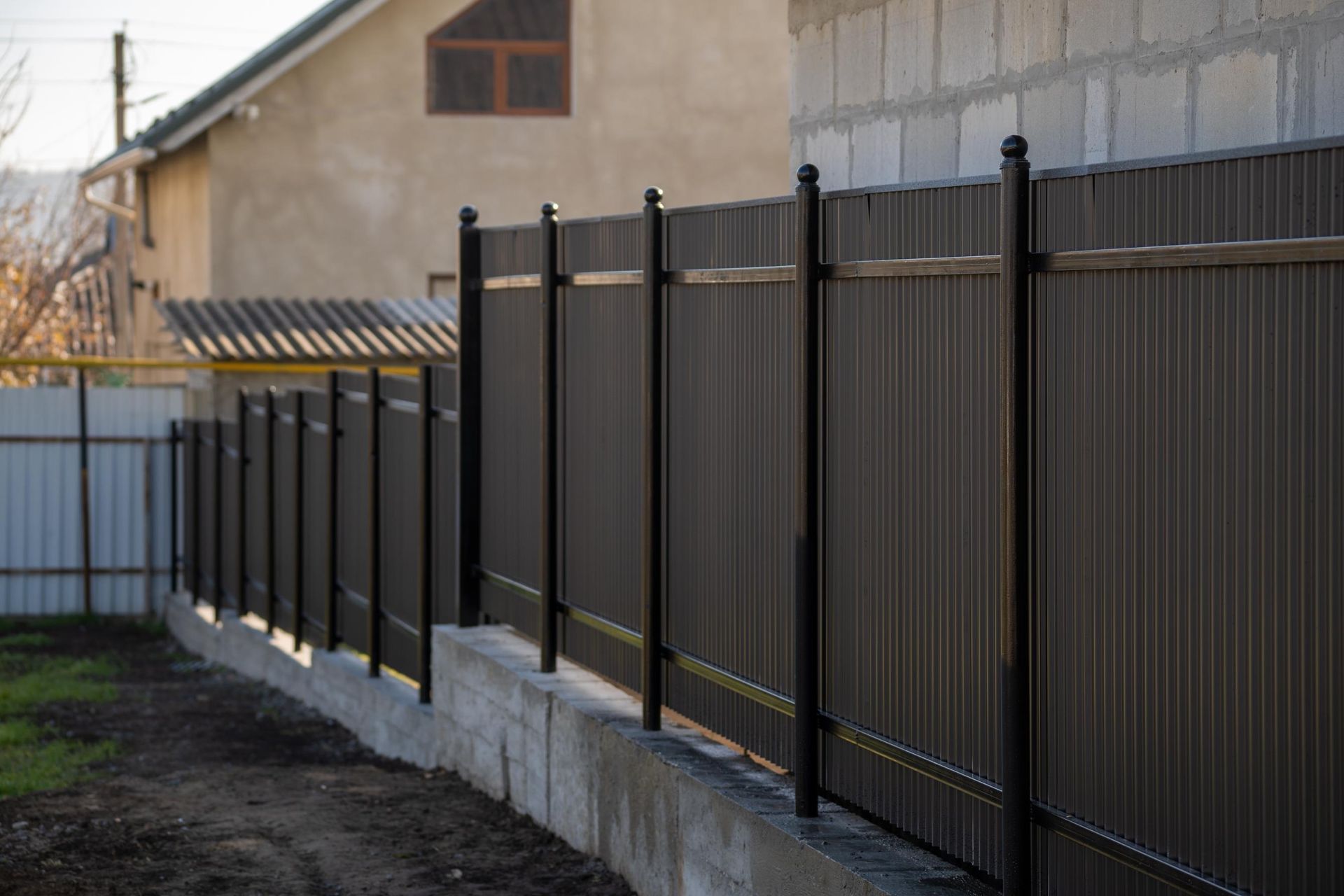 Dark brown metal fence on a concrete base, separating a yard from a building.