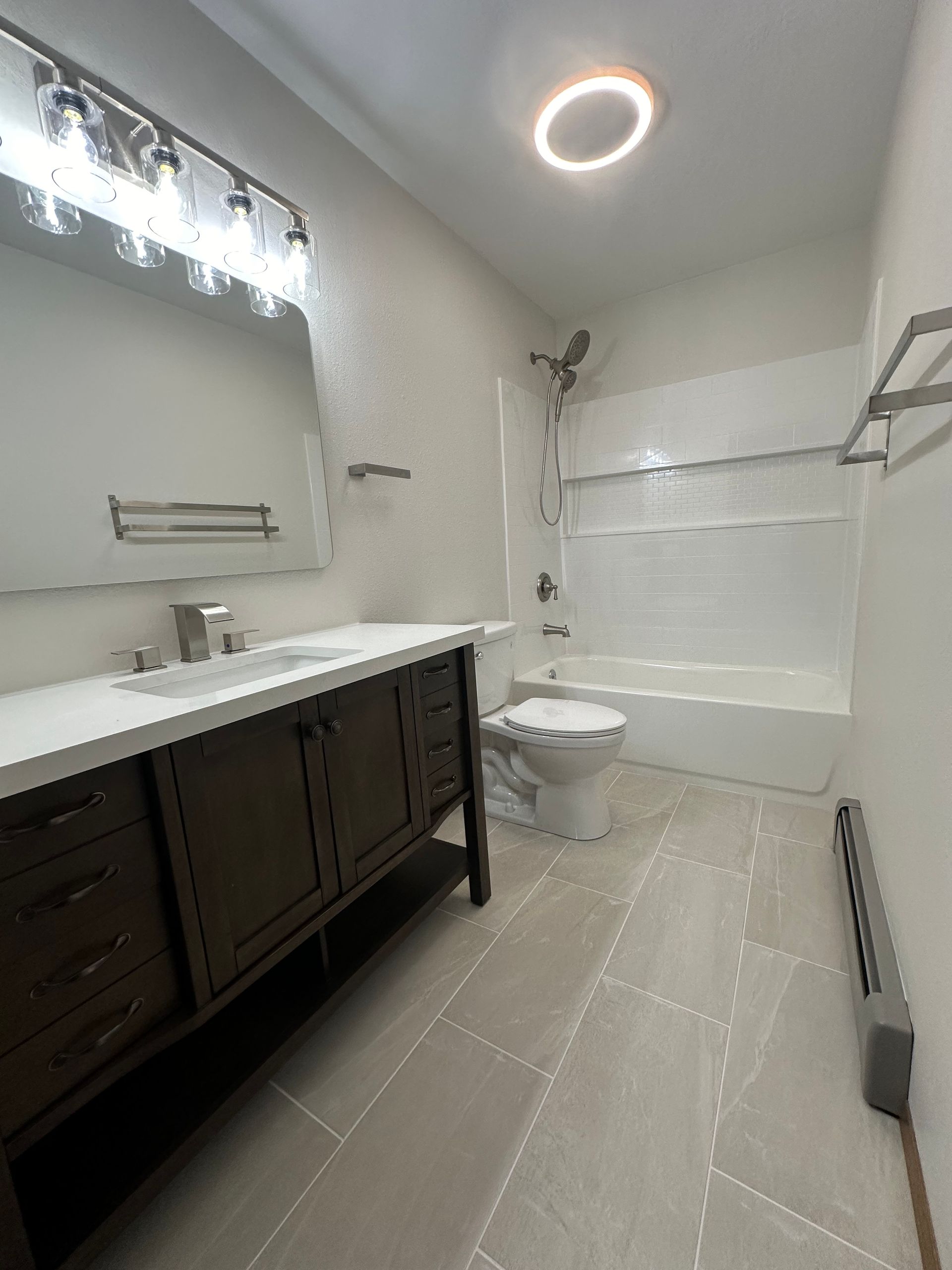 Bathroom with dark wood vanity, white countertop, tile floor, and tub/shower combo.