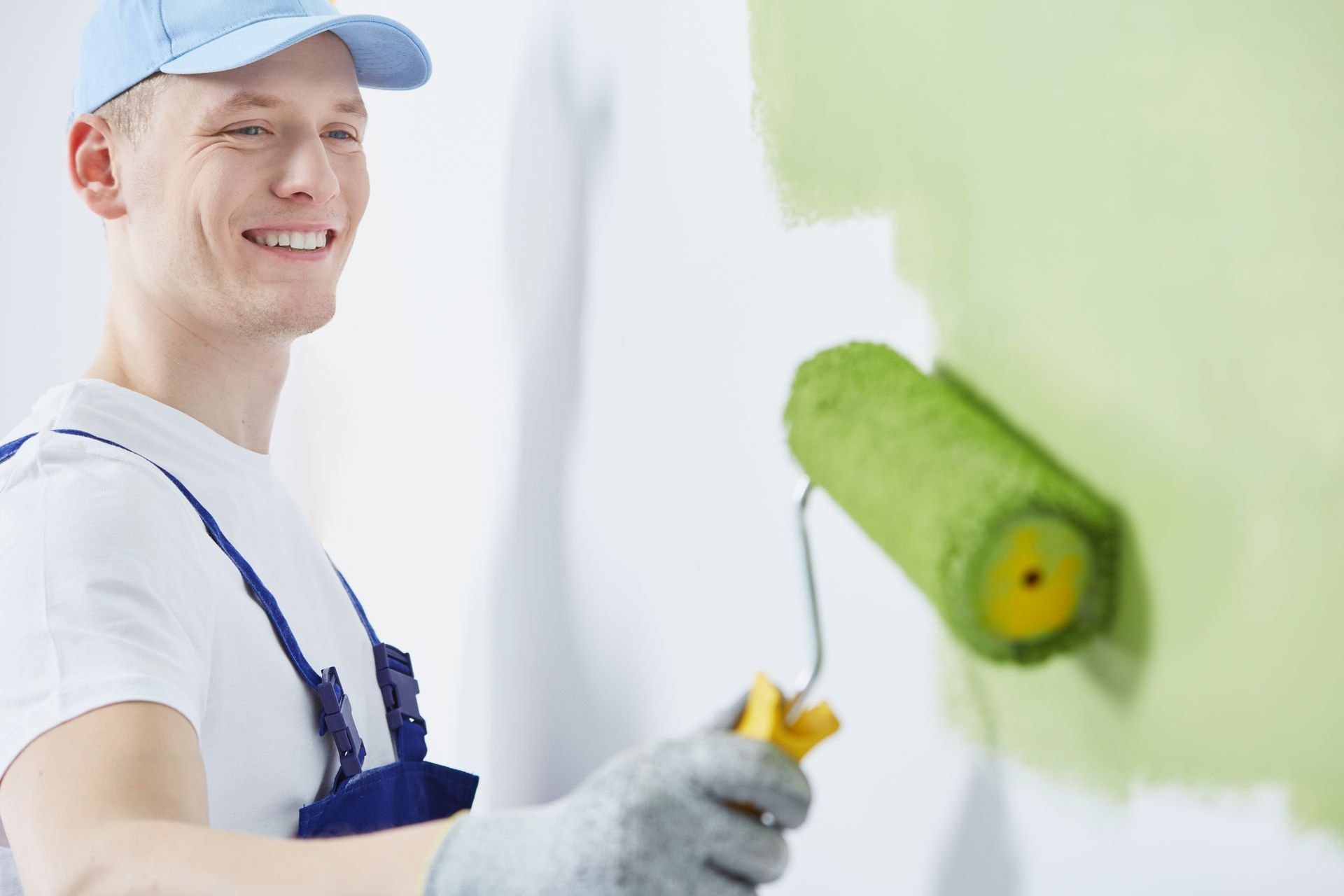 Painter rolling green paint on a wall with a paint roller, smiling in a bright room