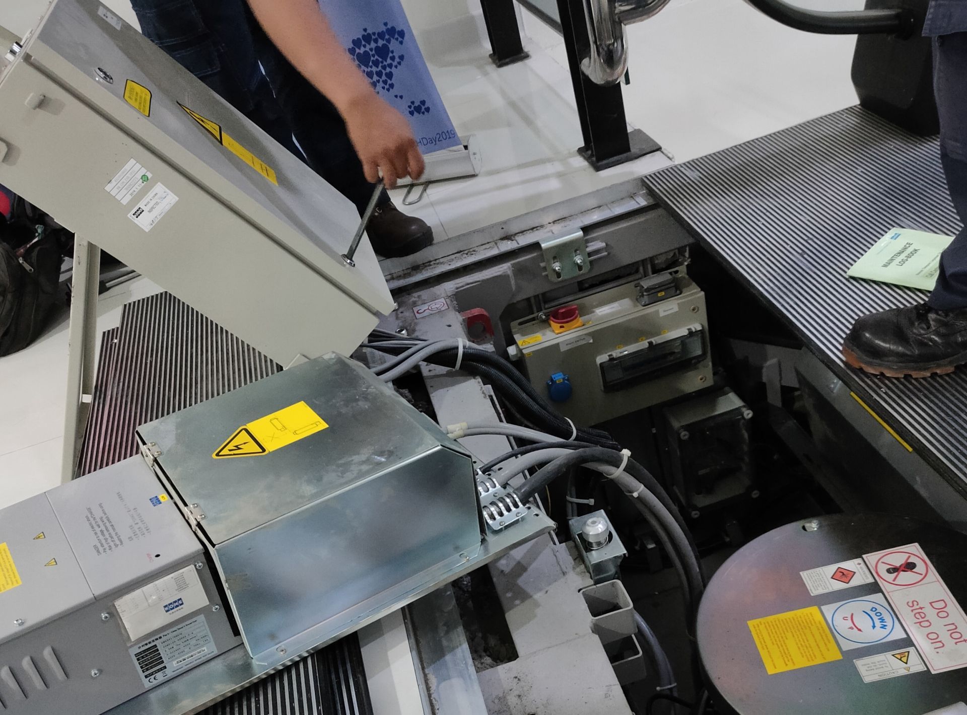 Factory machine interior with metal panels, hoses, and a worker's arm adjusting equipment.