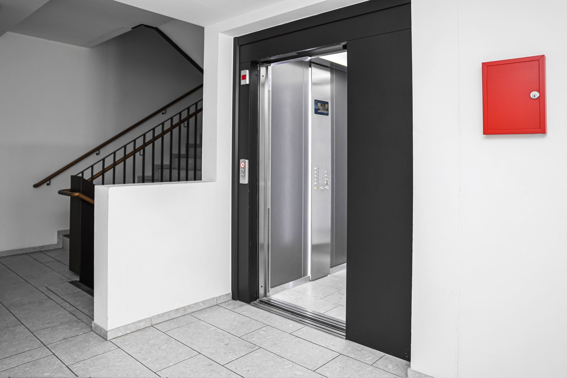 Open elevator in a building hallway beside a staircase and red wall box