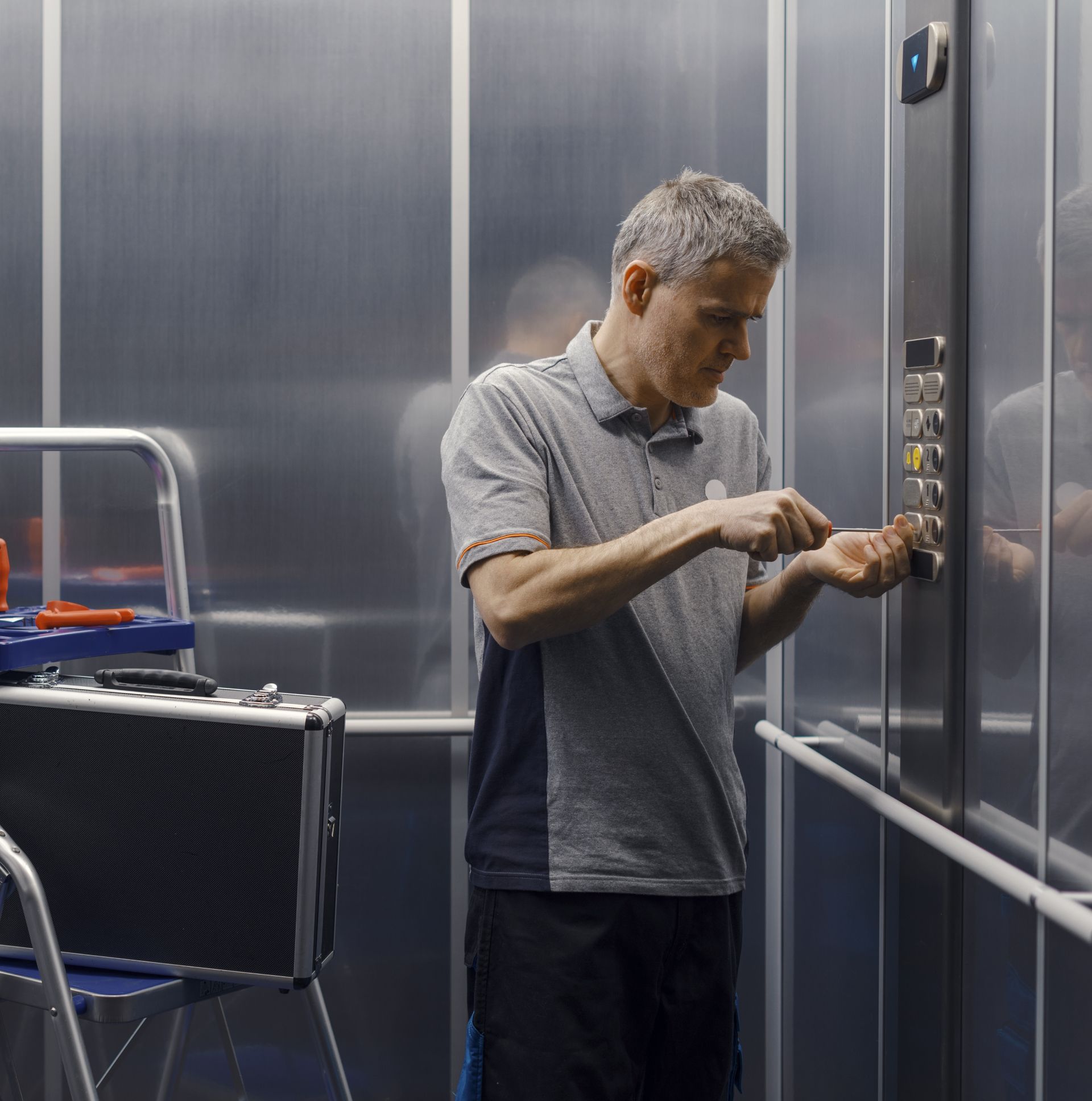 Man adjusting buttons in a stainless-steel elevator, standing beside a luggage cart.