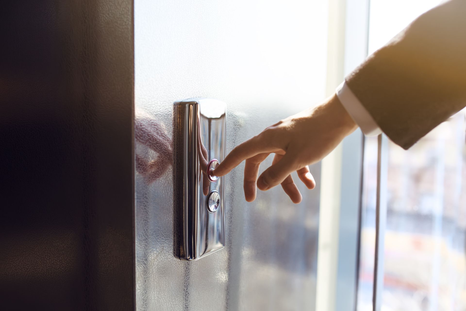 Hand reaching for a silver door handle on a glass door in bright sunlight
