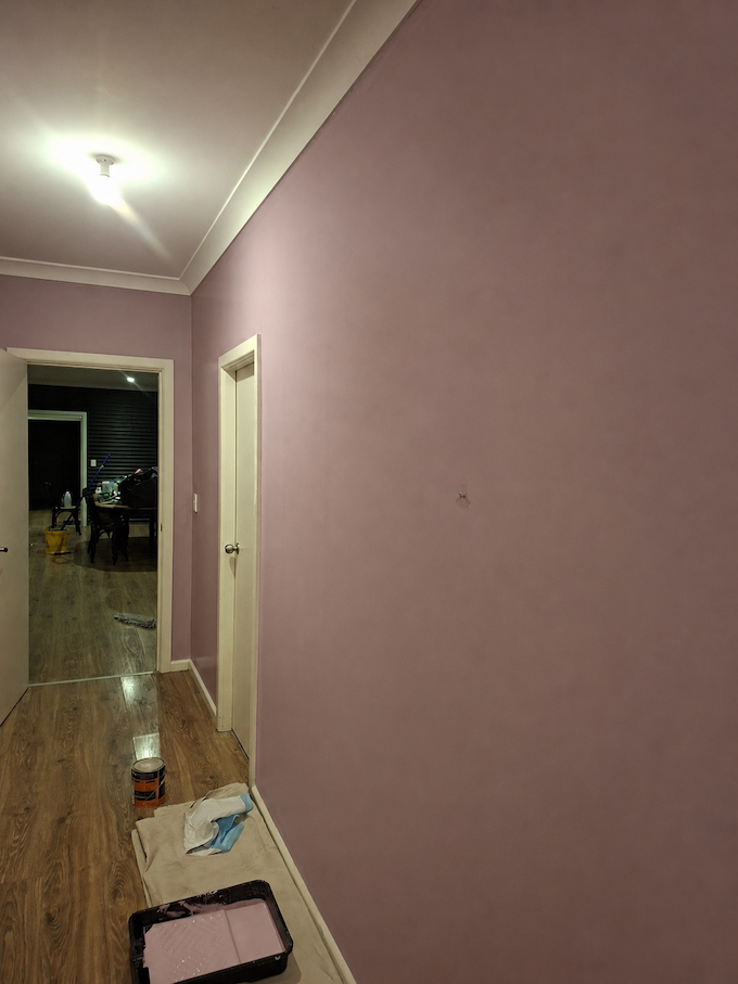 Pink hallway with a white door, ceiling light, and painting supplies on the floor leading into another room — Matty Stewart Painting & Decorating in Mudgee, NSW