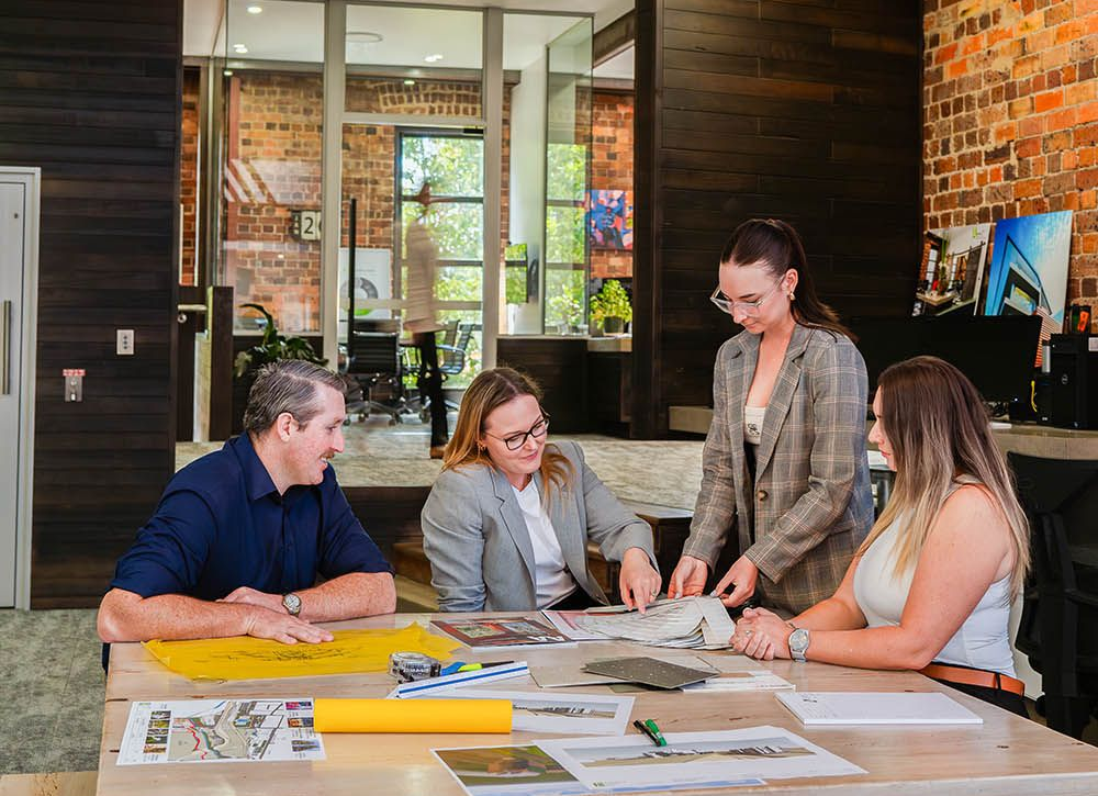 Four people in a meeting room reviewing plans spread across a table