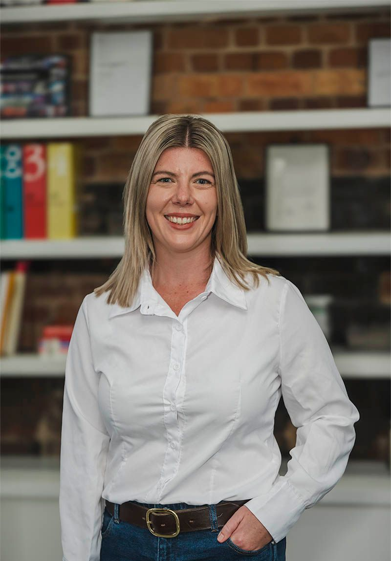 Woman in a white shirt smiling in front of shelves and a brick wall
