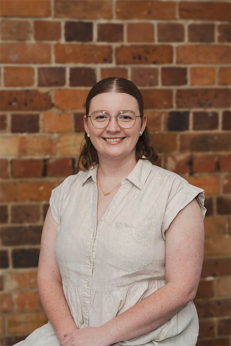 Smiling person in glasses and a light blouse standing before a brick wall