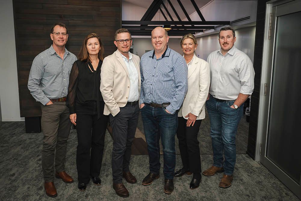Six people standing together in a modern office, posing for a group photo.