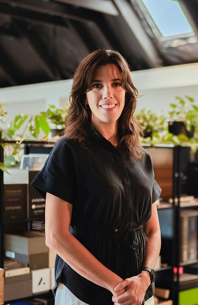 Woman in a black dress standing in a bright modern office, smiling at the camera.