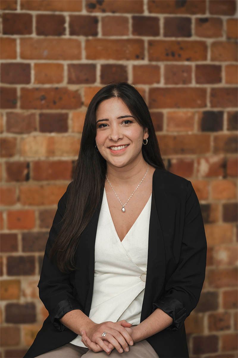 Portrait of a smiling woman in a black blazer and white top against a brick wall