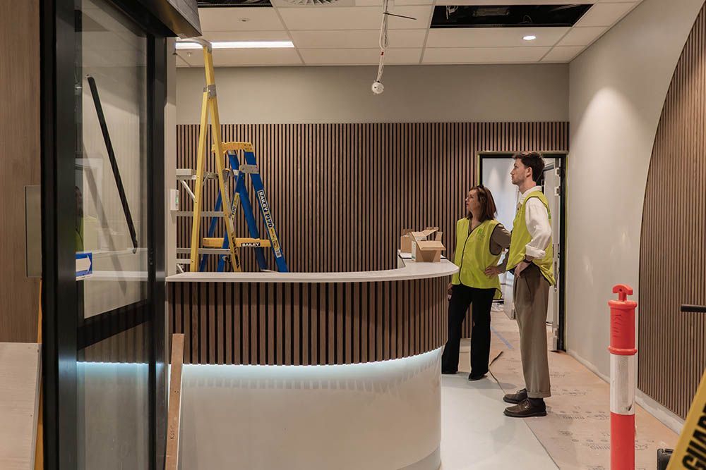 Lobby with two people standing near a curved reception desk and a ladder in the background