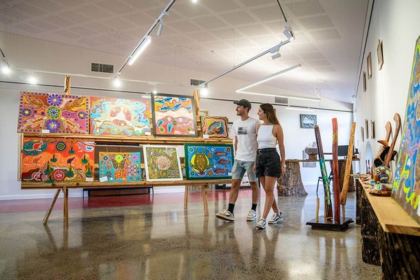 Art gallery with colorful paintings on display as two people examine the artwork.