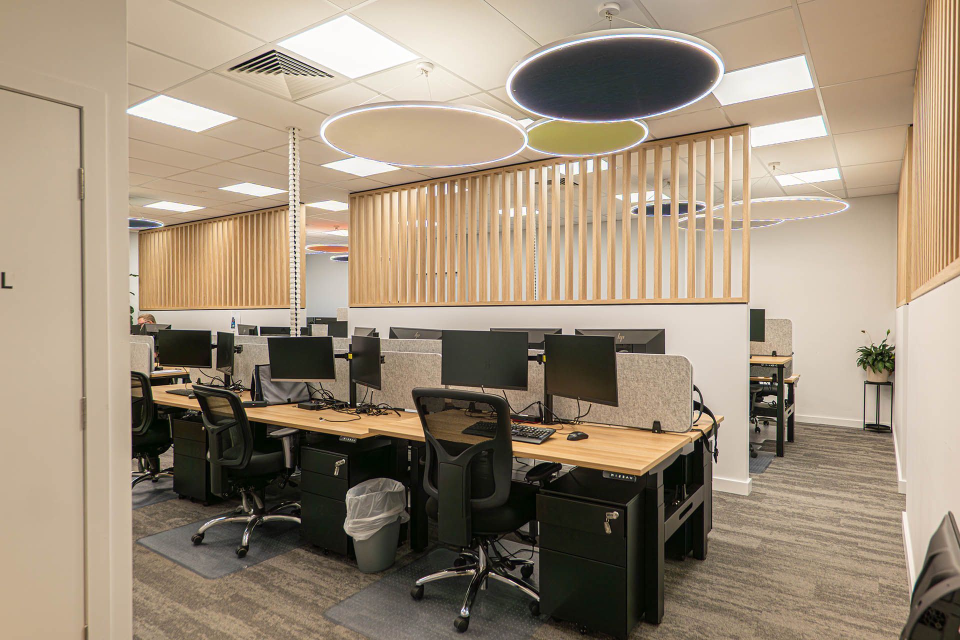 Open-plan office with desks, computer monitors, rolling chairs, and circular ceiling lights