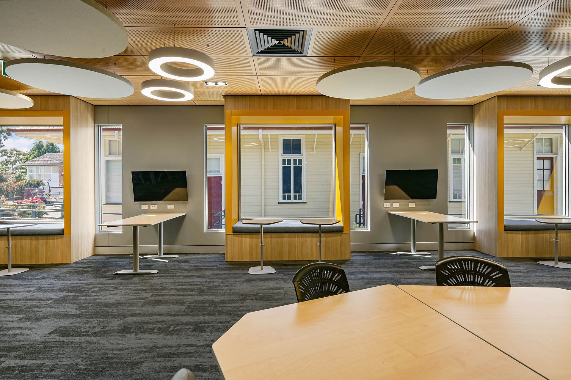 Modern lounge with patterned ceiling, wall-mounted screens, tables, and large windows