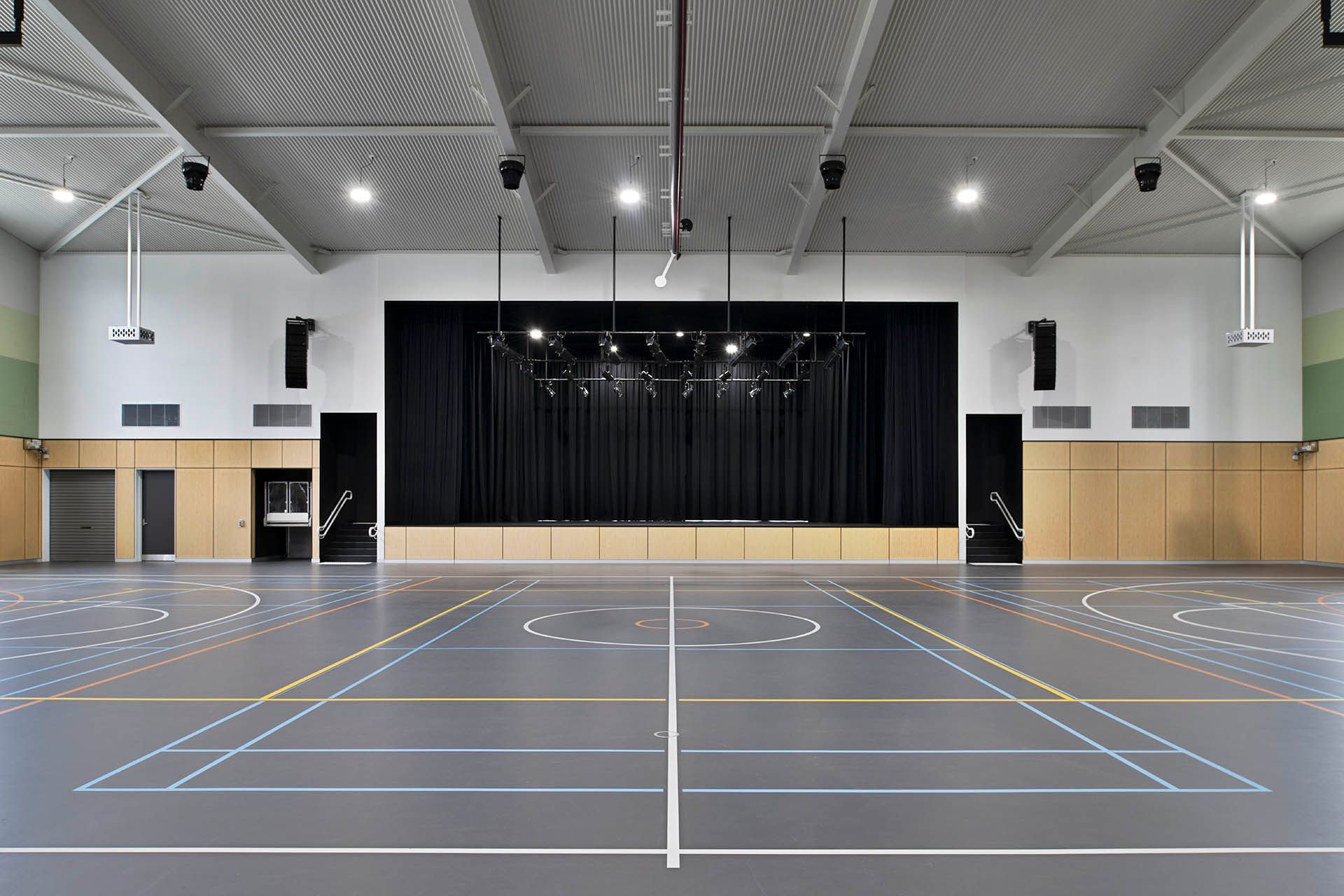 Empty indoor sports hall with a stage at the far end and marked gray court flooring
