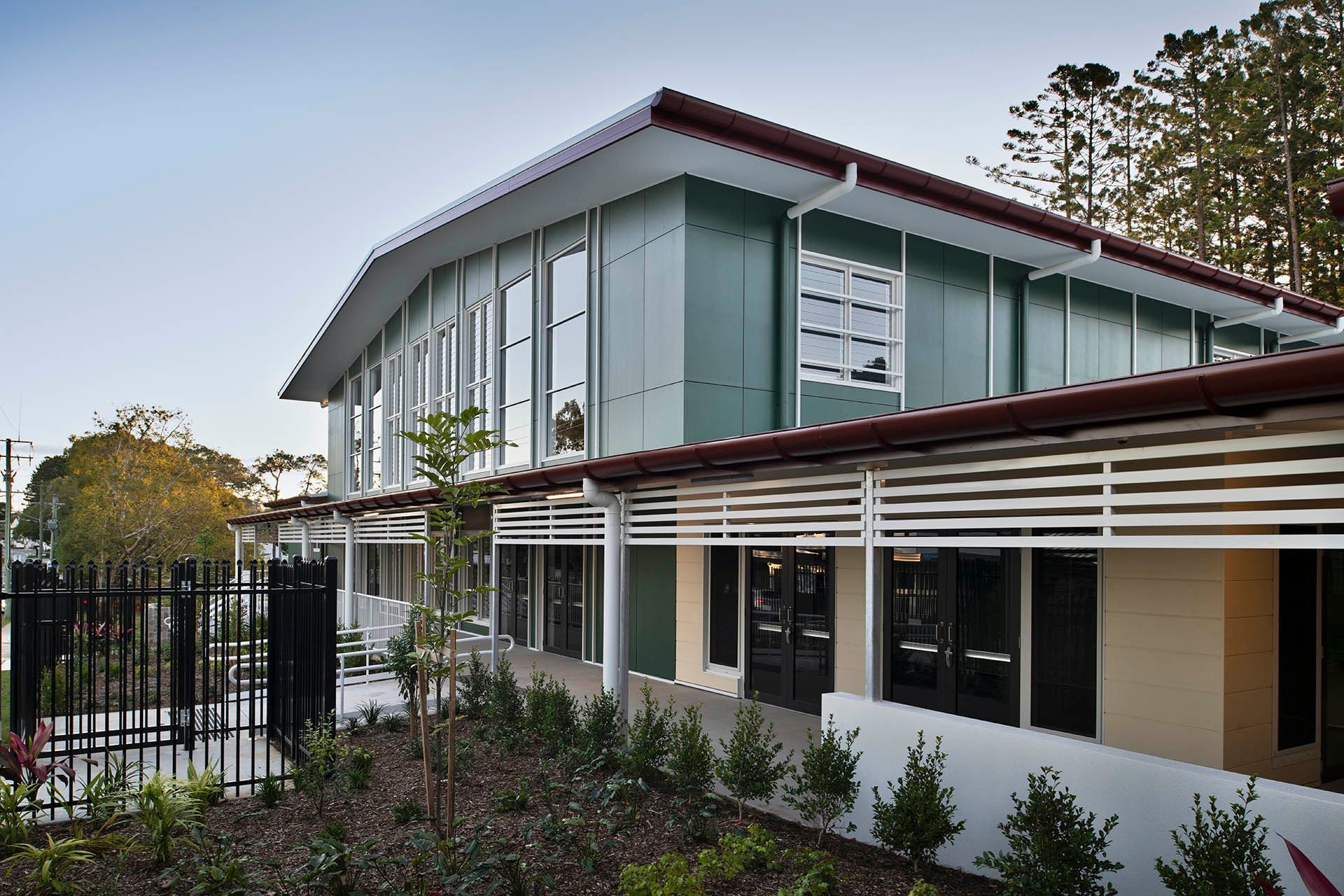 Modern two-story house with glass upper windows, white walls, and a red roof, seen from a garden path
