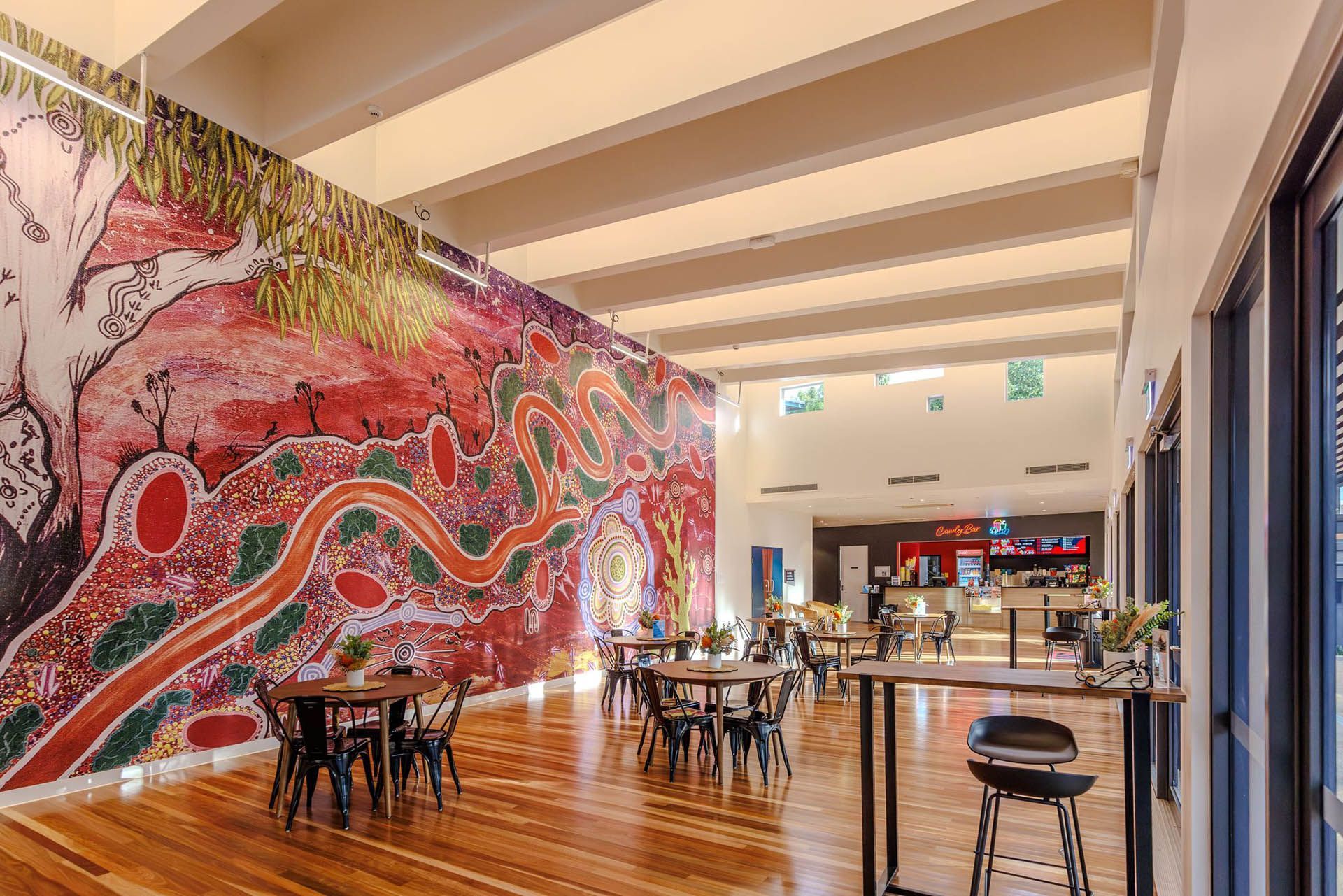 Modern restaurant interior with a colorful mural, wooden floors, and tables set for dining