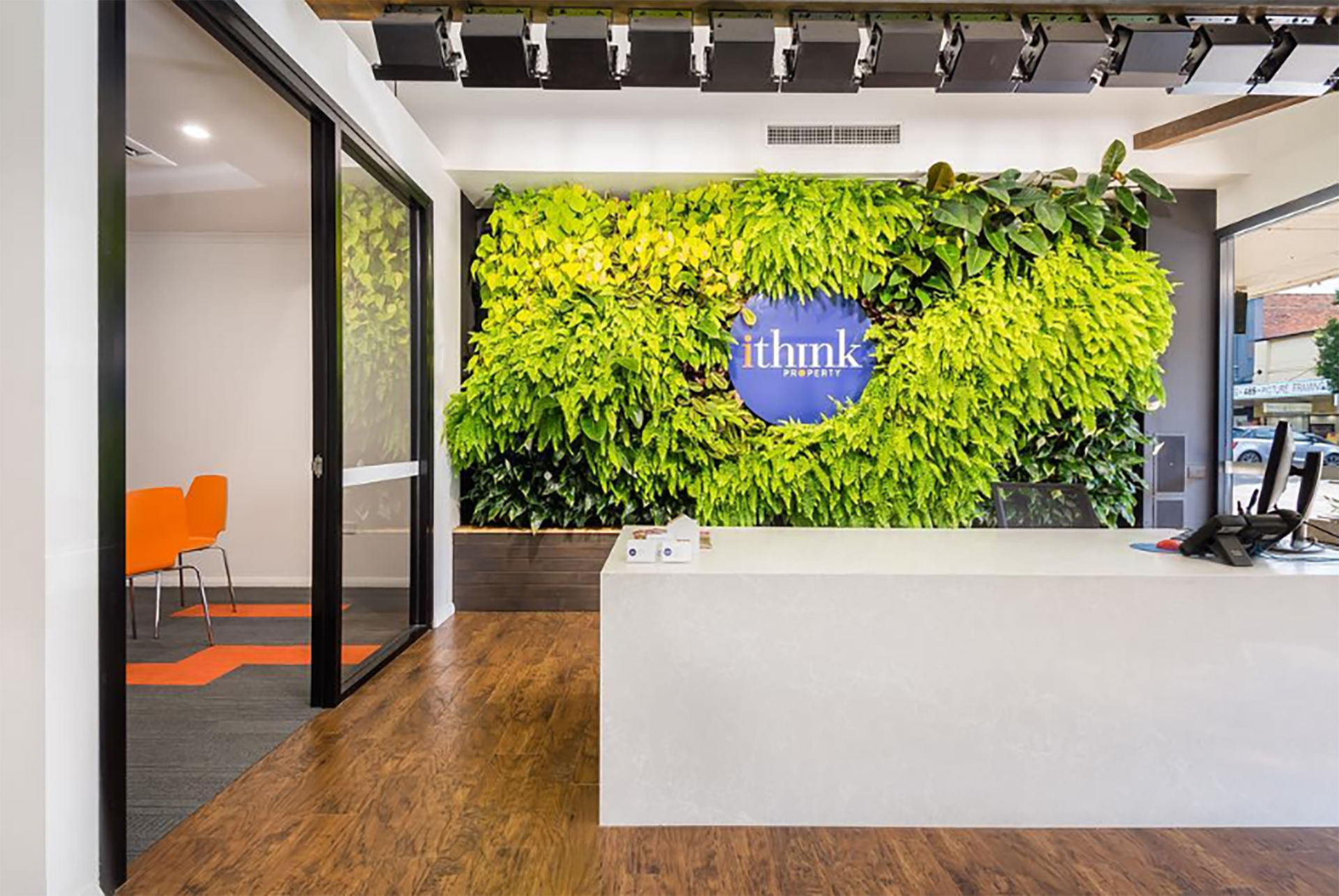 Modern office lobby with green plant wall, white reception desk, and glass-walled meeting room