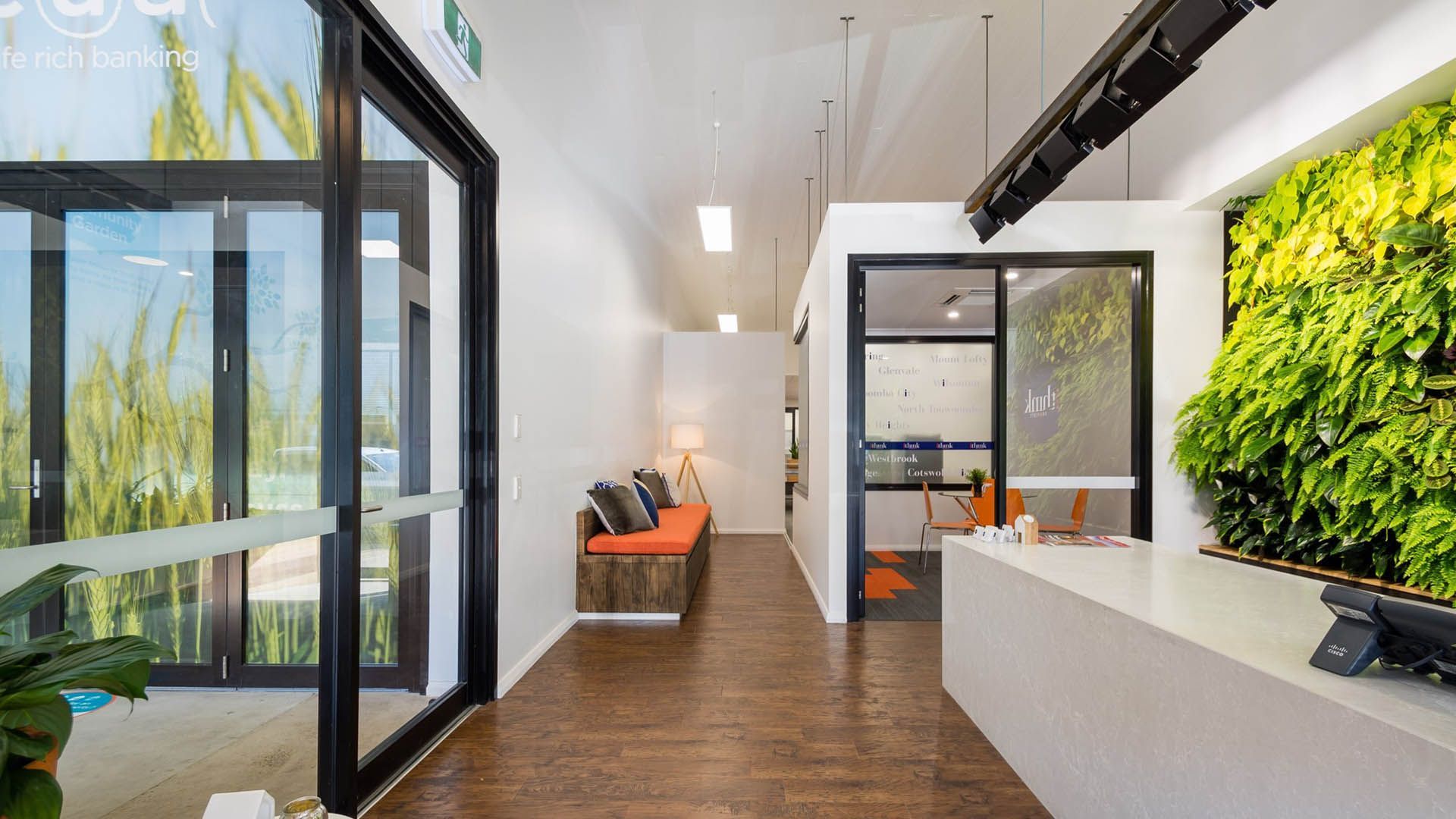 Modern office hallway with glass doors, wood floors, white walls, and a green plant wall