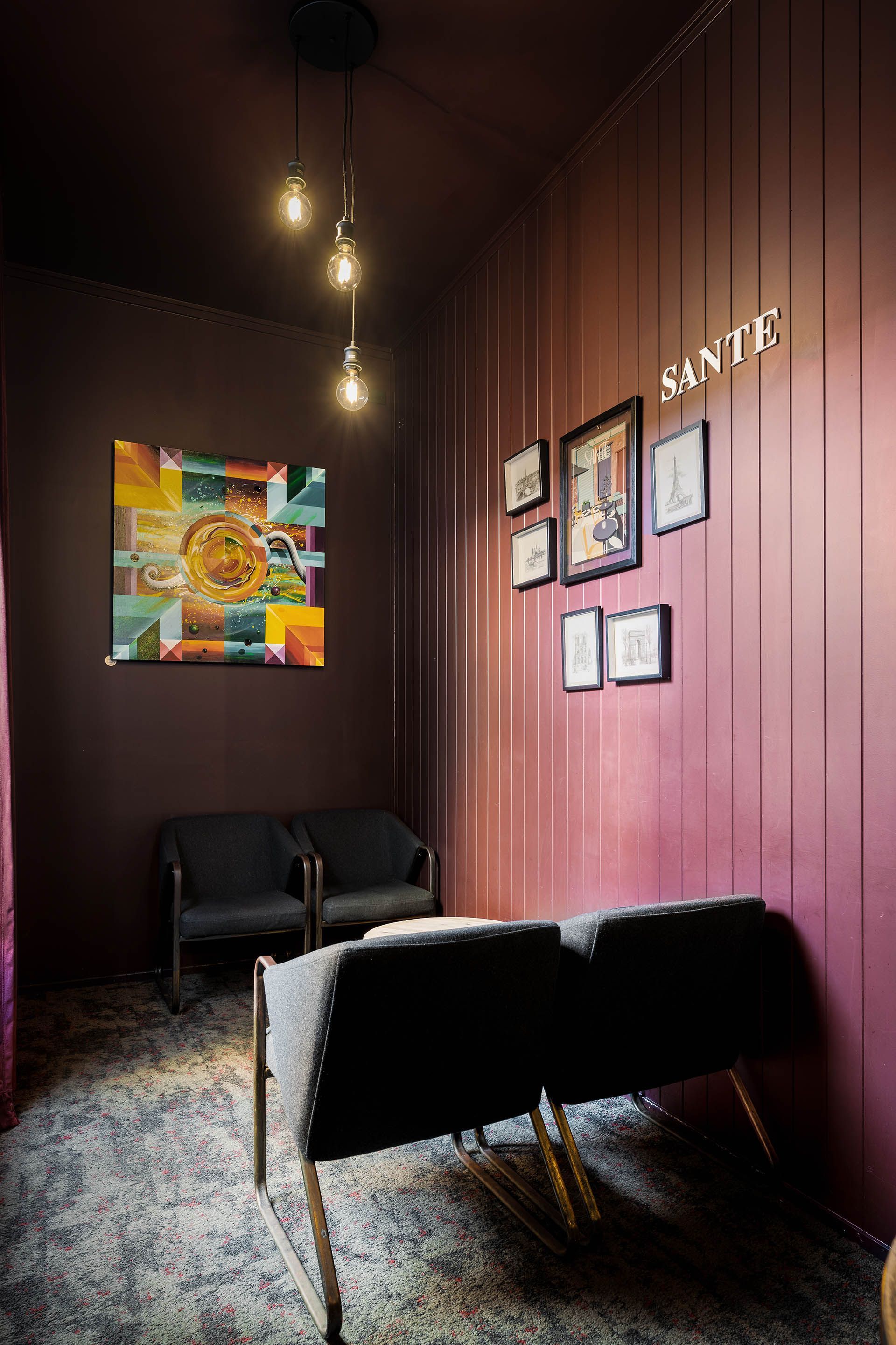 Dim lounge with maroon walls, hanging bulbs, black chairs, framed art, and a shaggy rug.