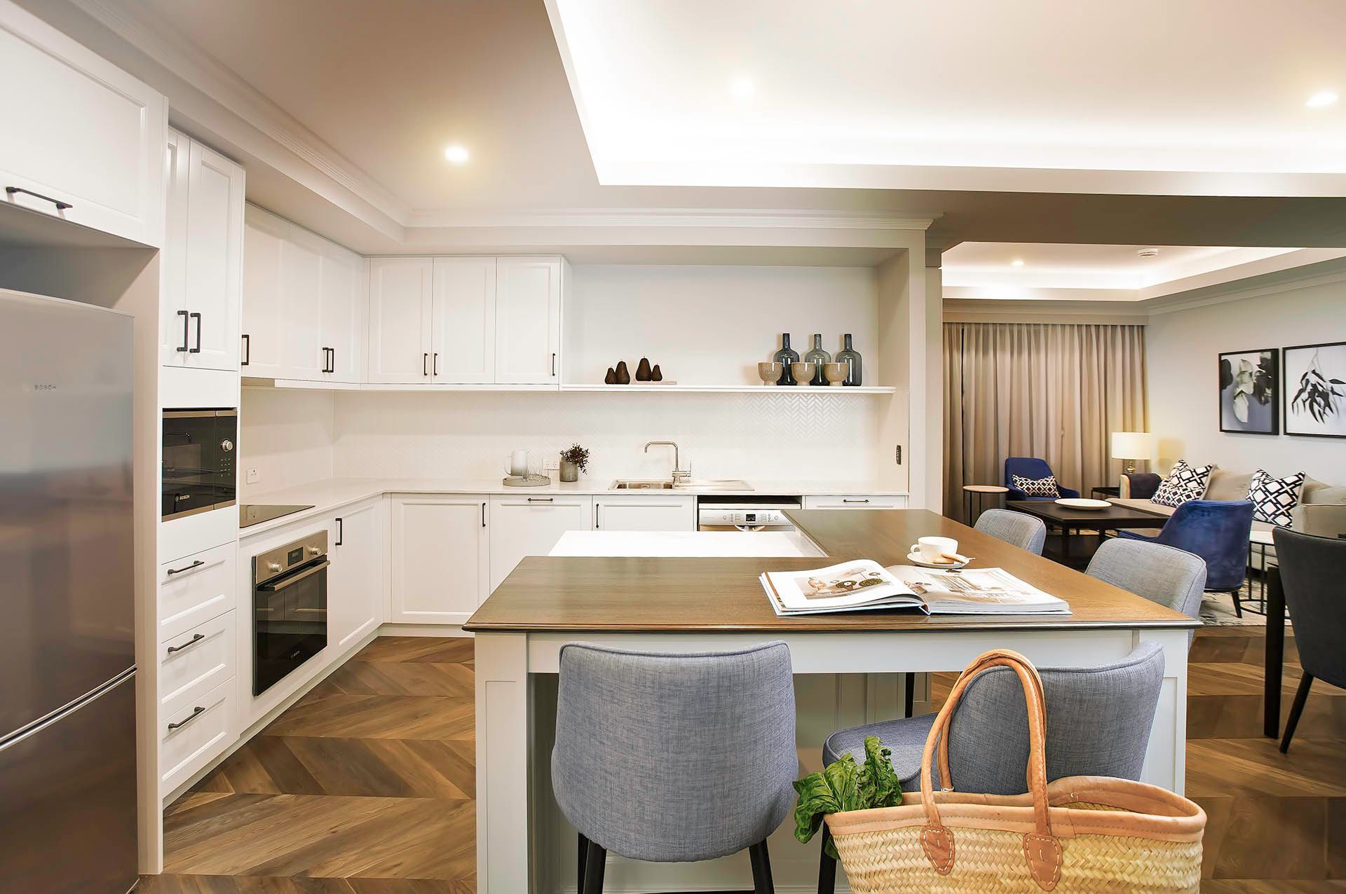 Bright modern kitchen with white cabinets, island, stools, and a view into a living room