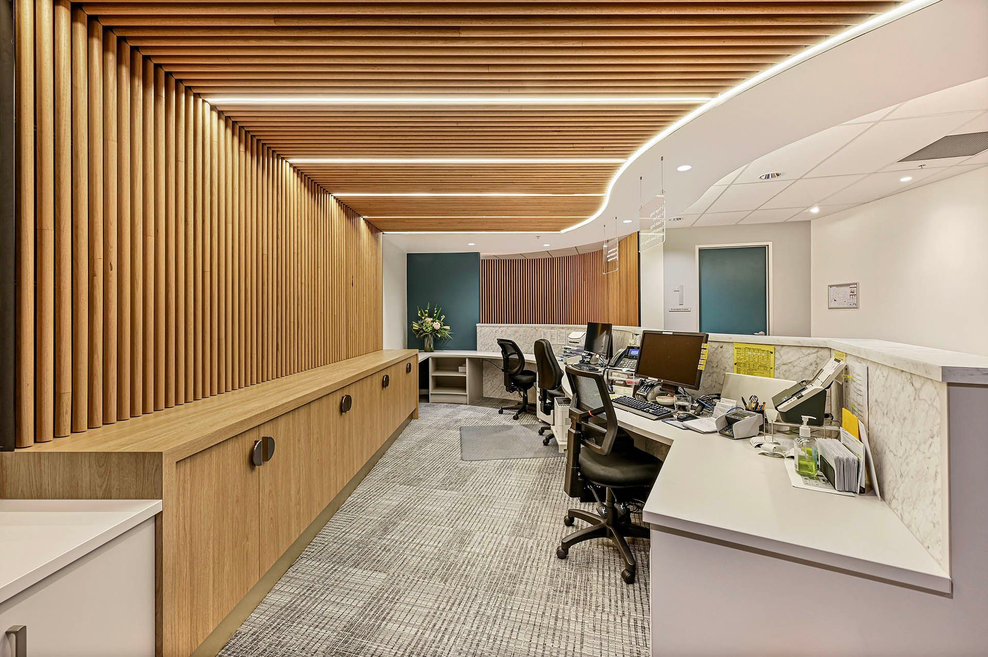 Modern office reception area with wood slat wall, white desk, and black chairs