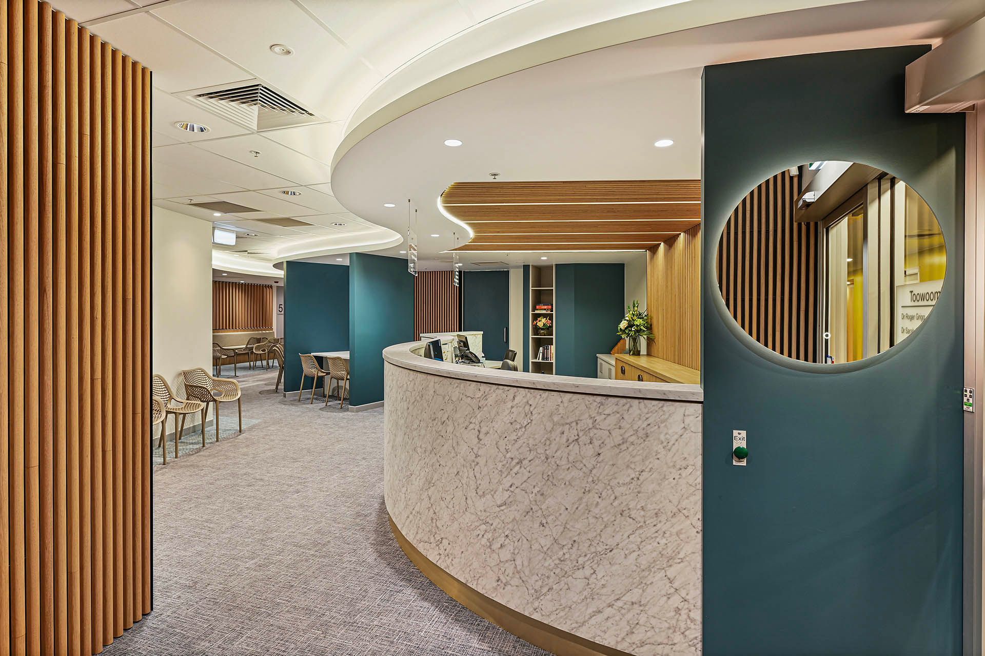 Modern reception area with curved white desk, teal walls, wood slats, and carpeted floor