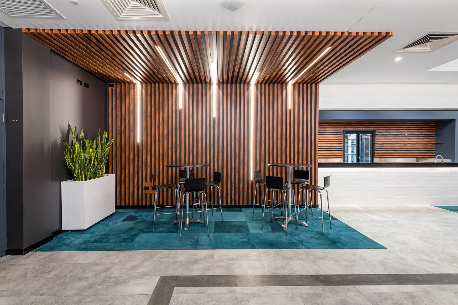 Modern lobby seating area with wood slat feature wall, blue rug, and white reception counter