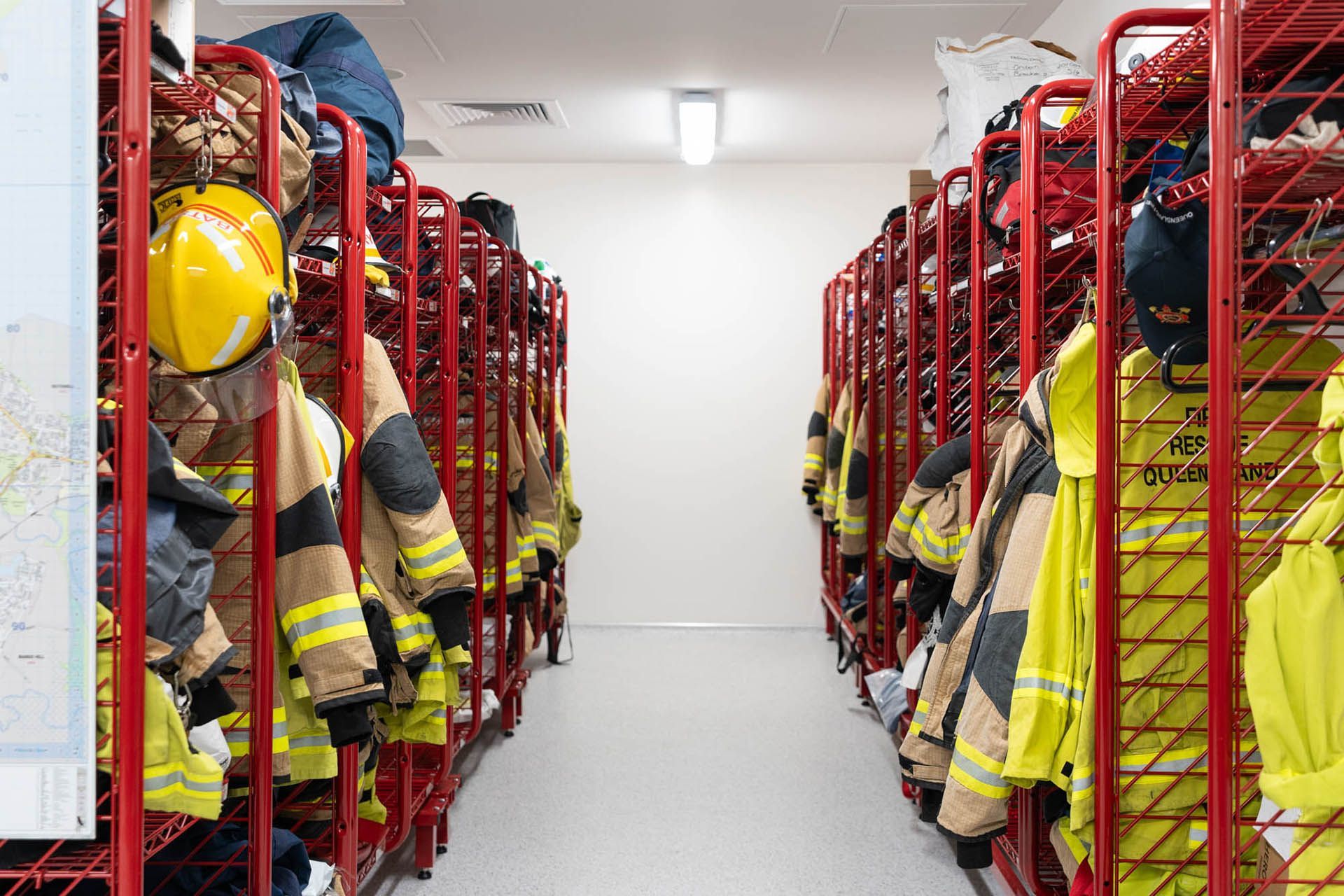 Fire station gear room with rows of red lockers holding yellow firefighting jackets and helmets