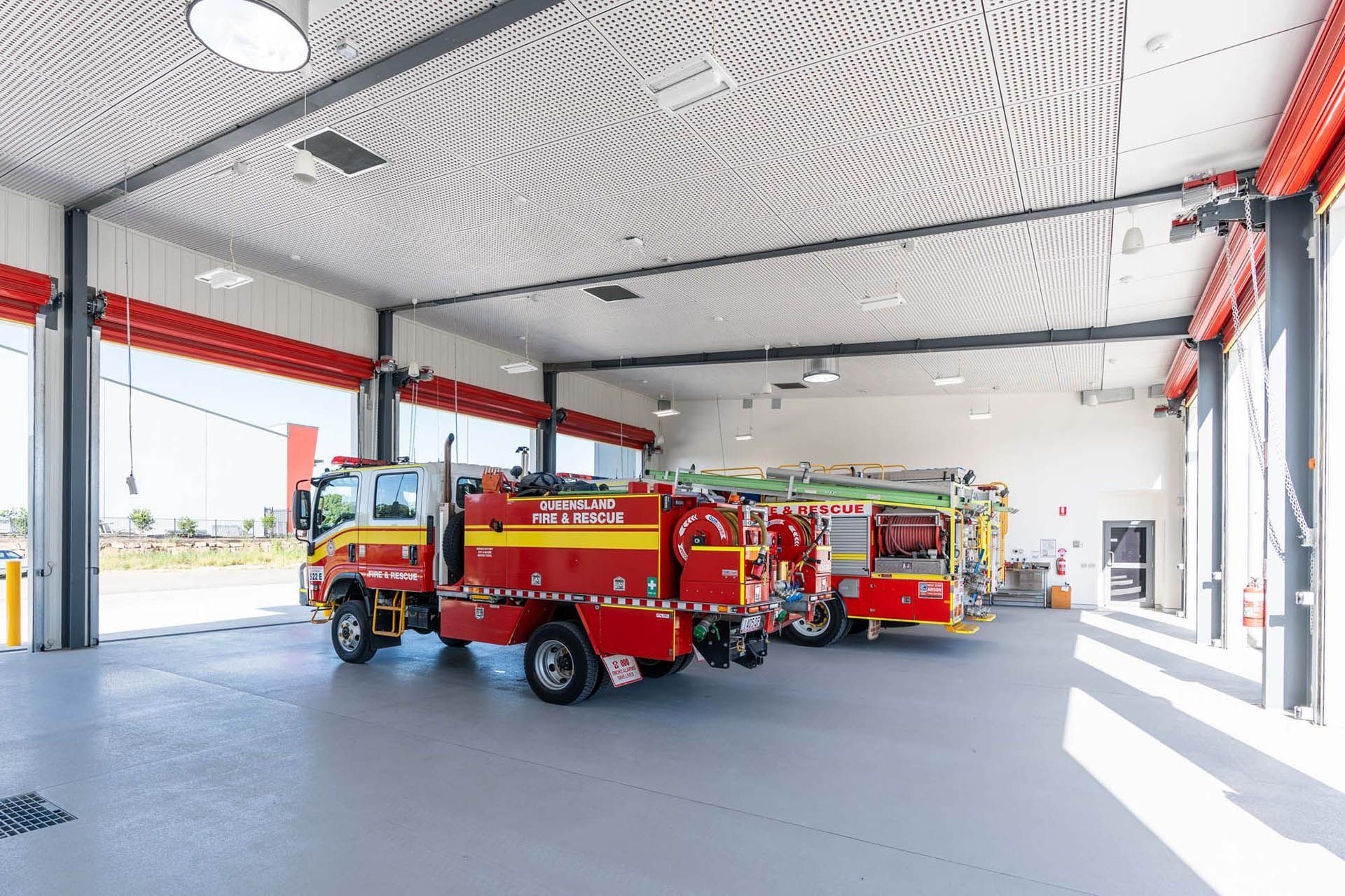 Red fire trucks parked inside a modern fire station bay with open doors and bright daylight.