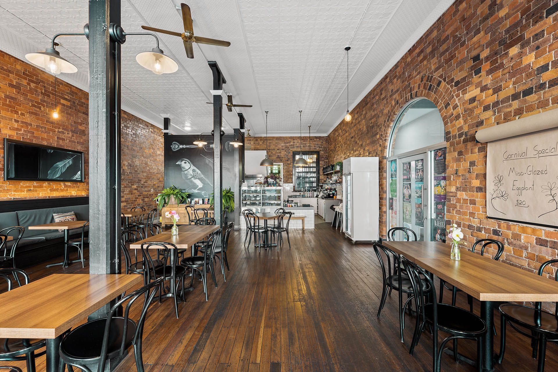 Empty café interior with brick walls, wooden floors, and tables along a bright aisle